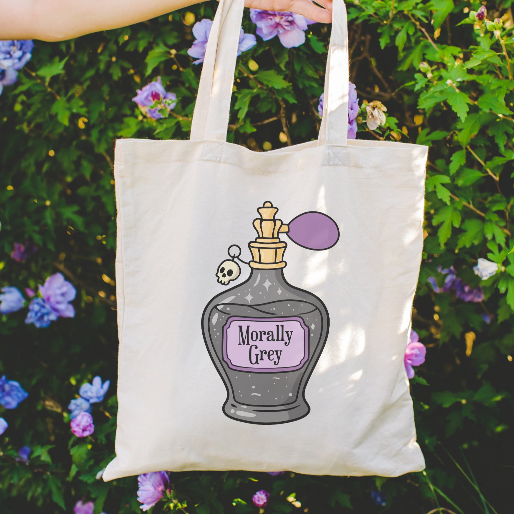 bookish Tote bag with 'Morally Grey' design held in front of a floral background