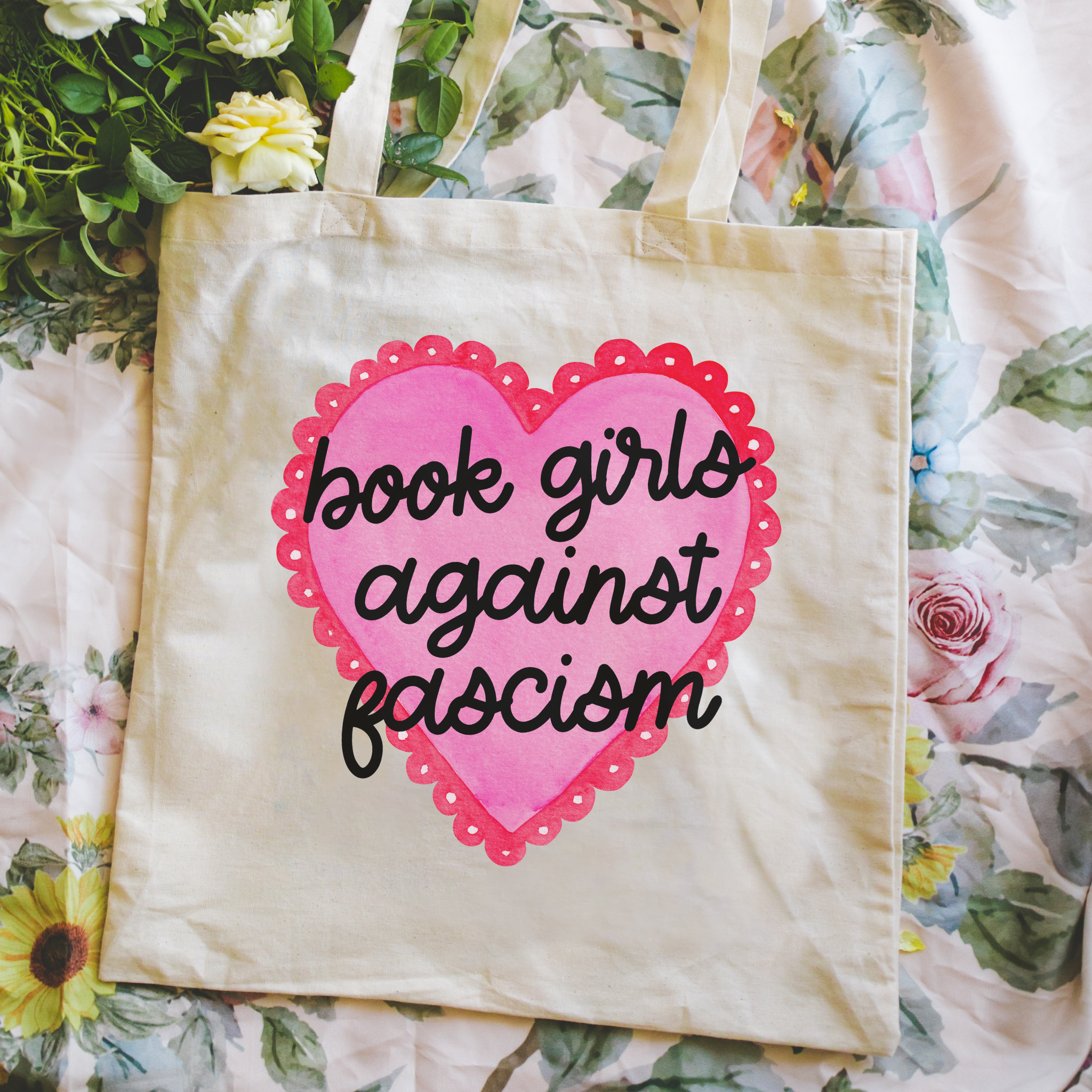 Tote bag with pink heart and text 'book girls against fascism' on a floral background