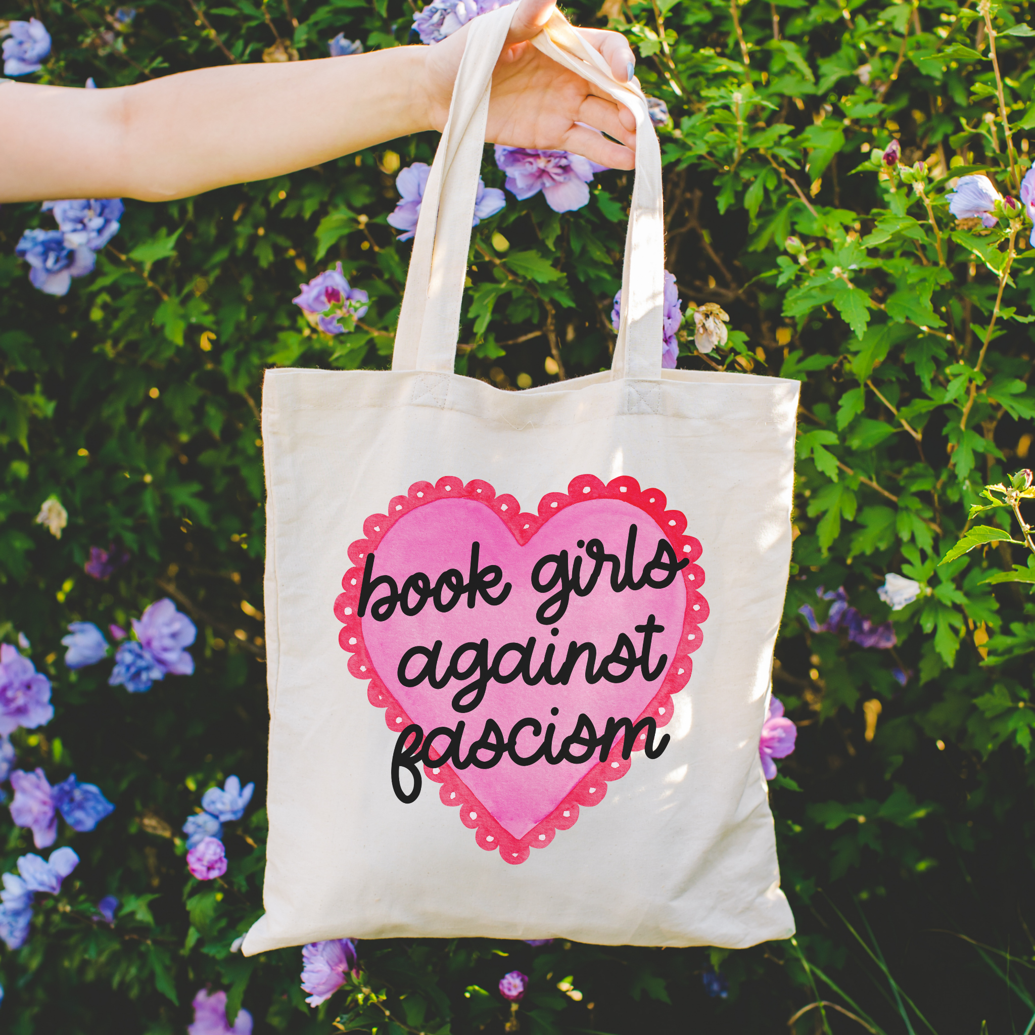 Tote bag with 'book girls against fascism' design held in front of a floral background