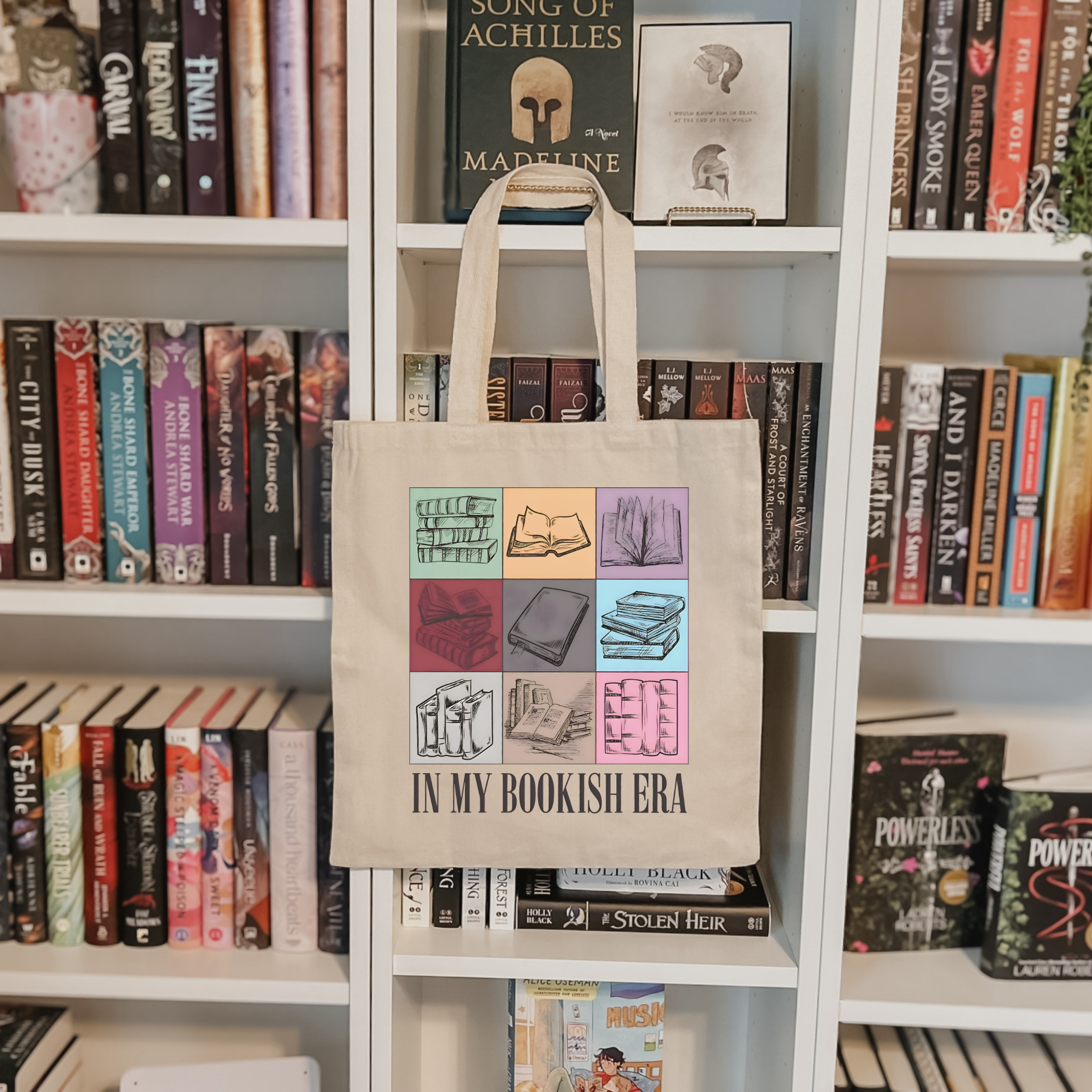 Tote bag with book-themed design in front of a bookshelf filled with books.