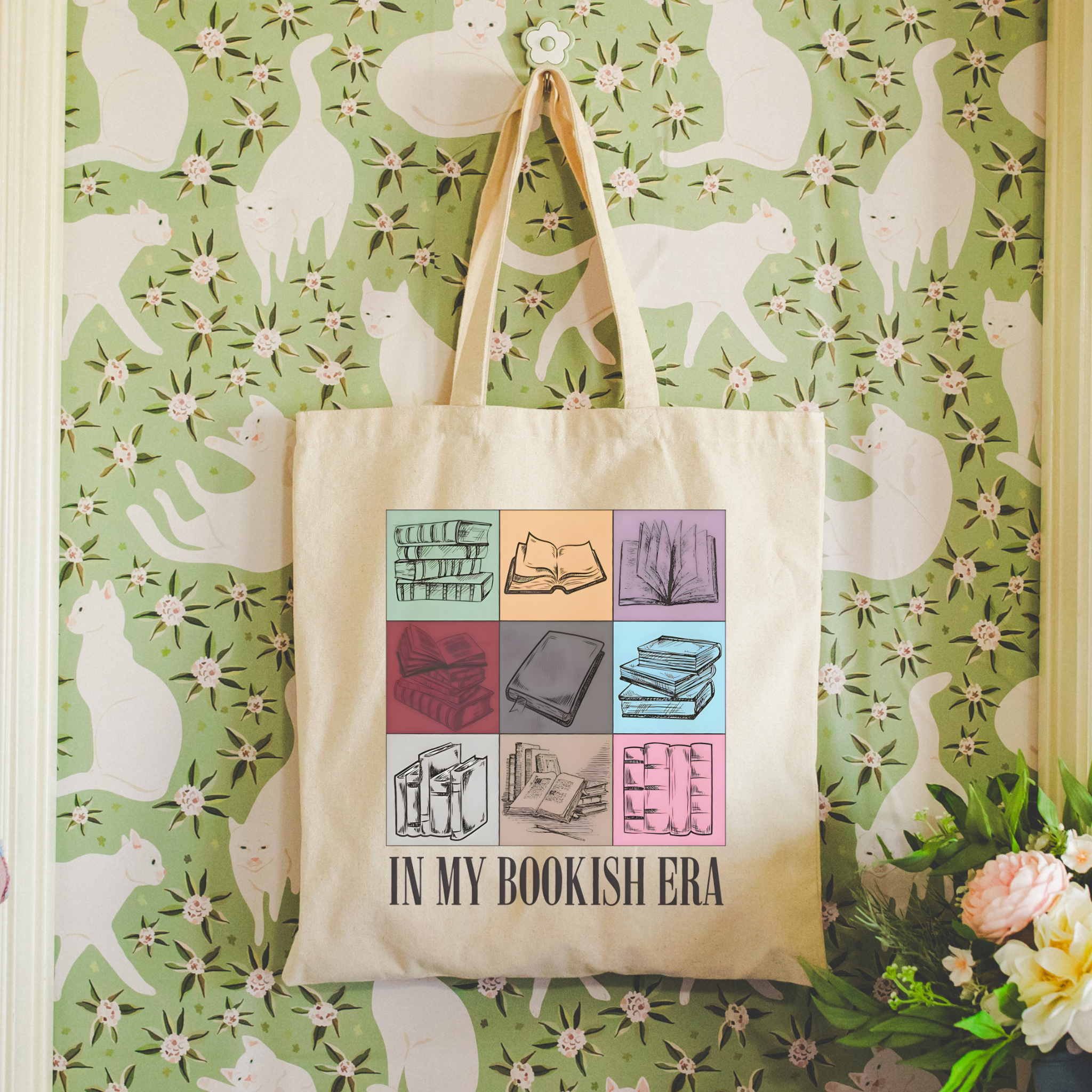 Tote bag with book design and text 'In My Bookish Era' hanging on a floral-patterned wall.