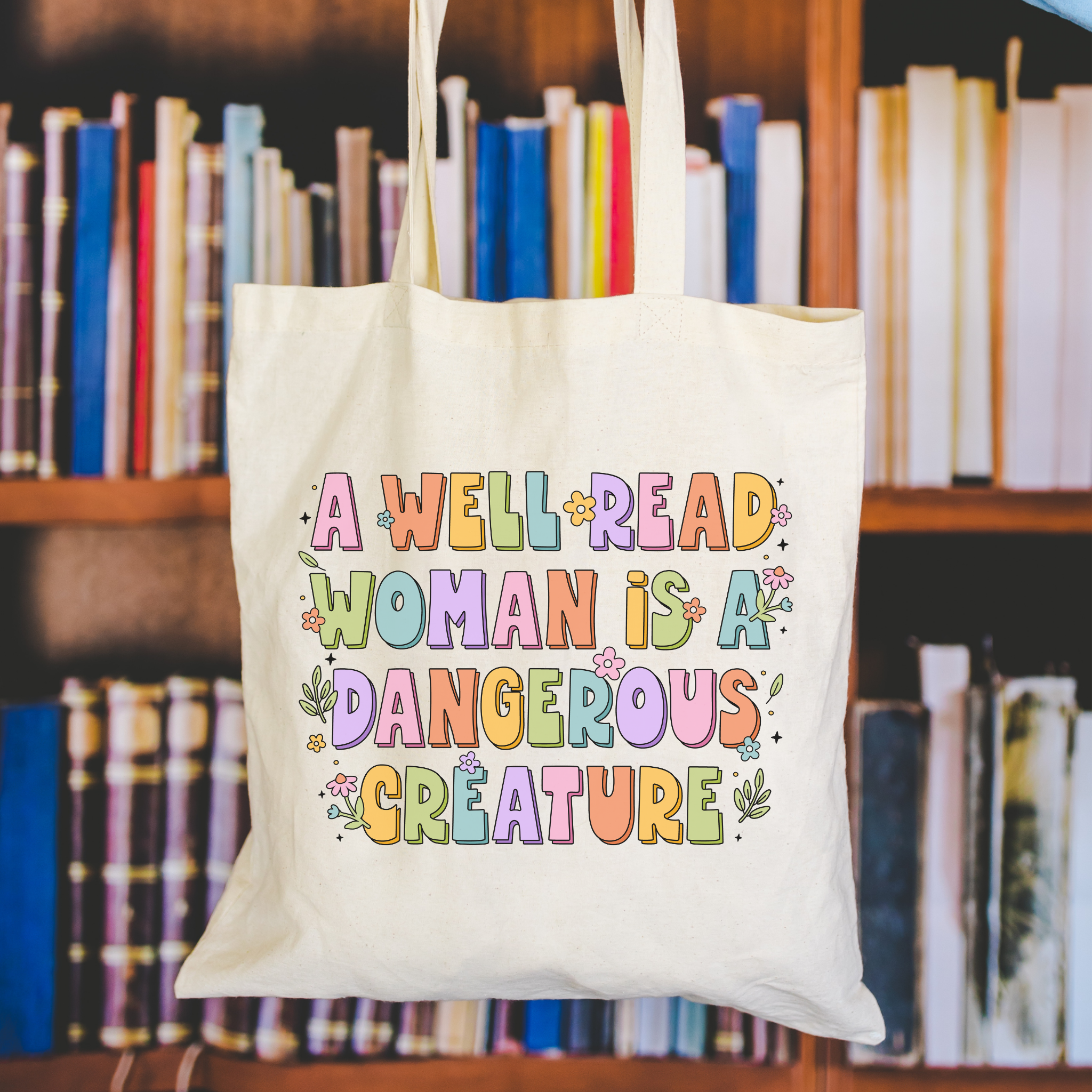 Tote bag with colorful text 'A Well Read Woman is a Dangerous Creature' in front of bookshelf