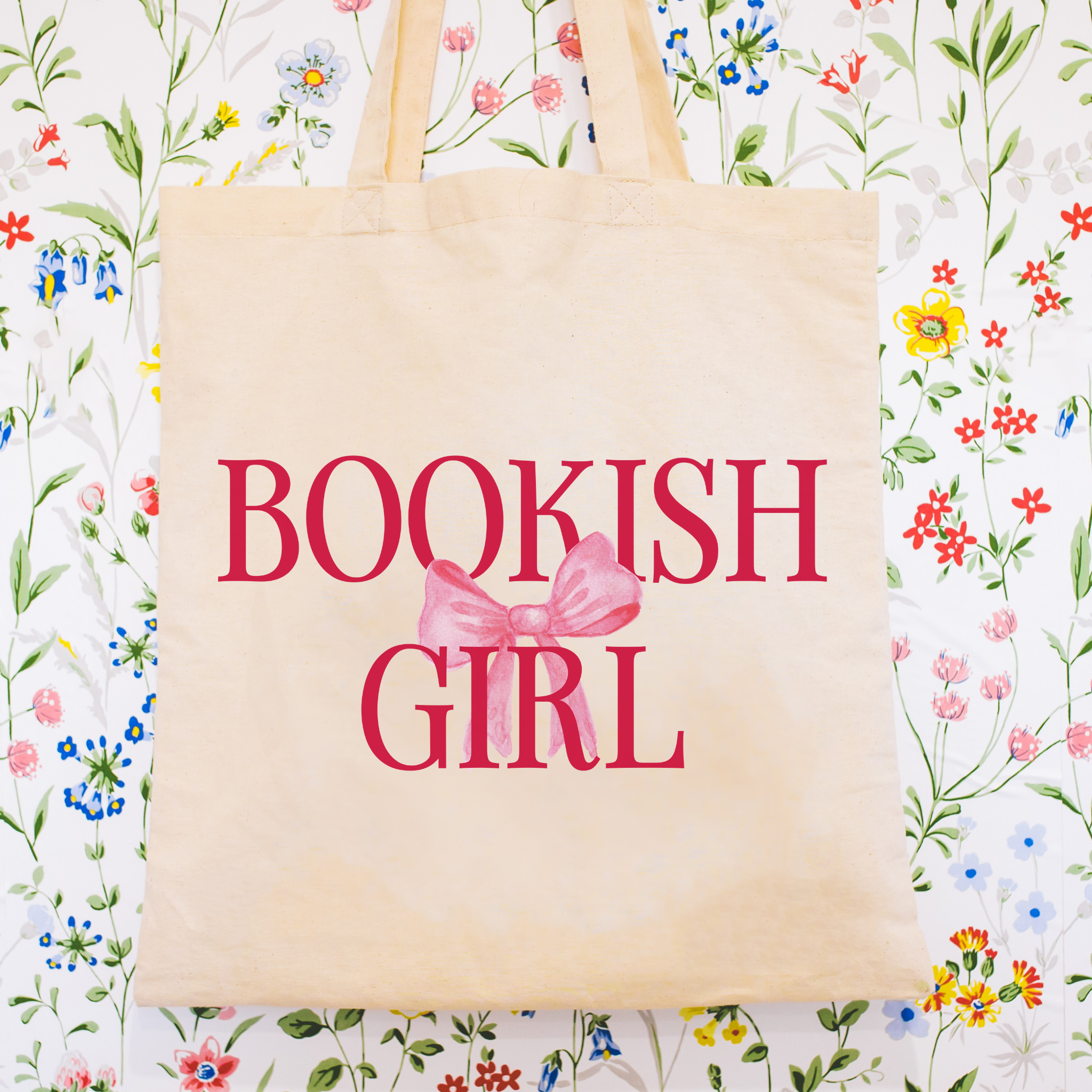 Beige tote bag with 'BOOKISH GIRL' text and pink bow on a floral background