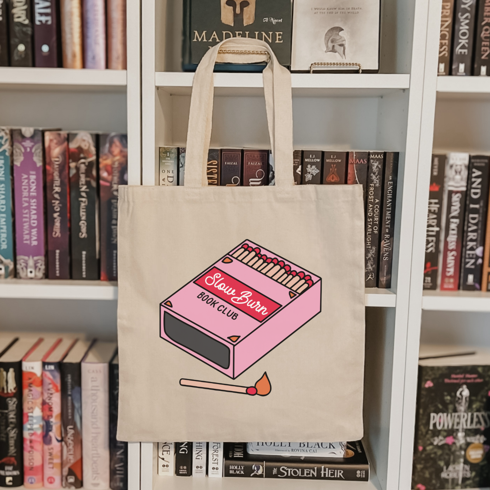 Bookish trope tote bag with pink matchbox design in front of a bookshelf