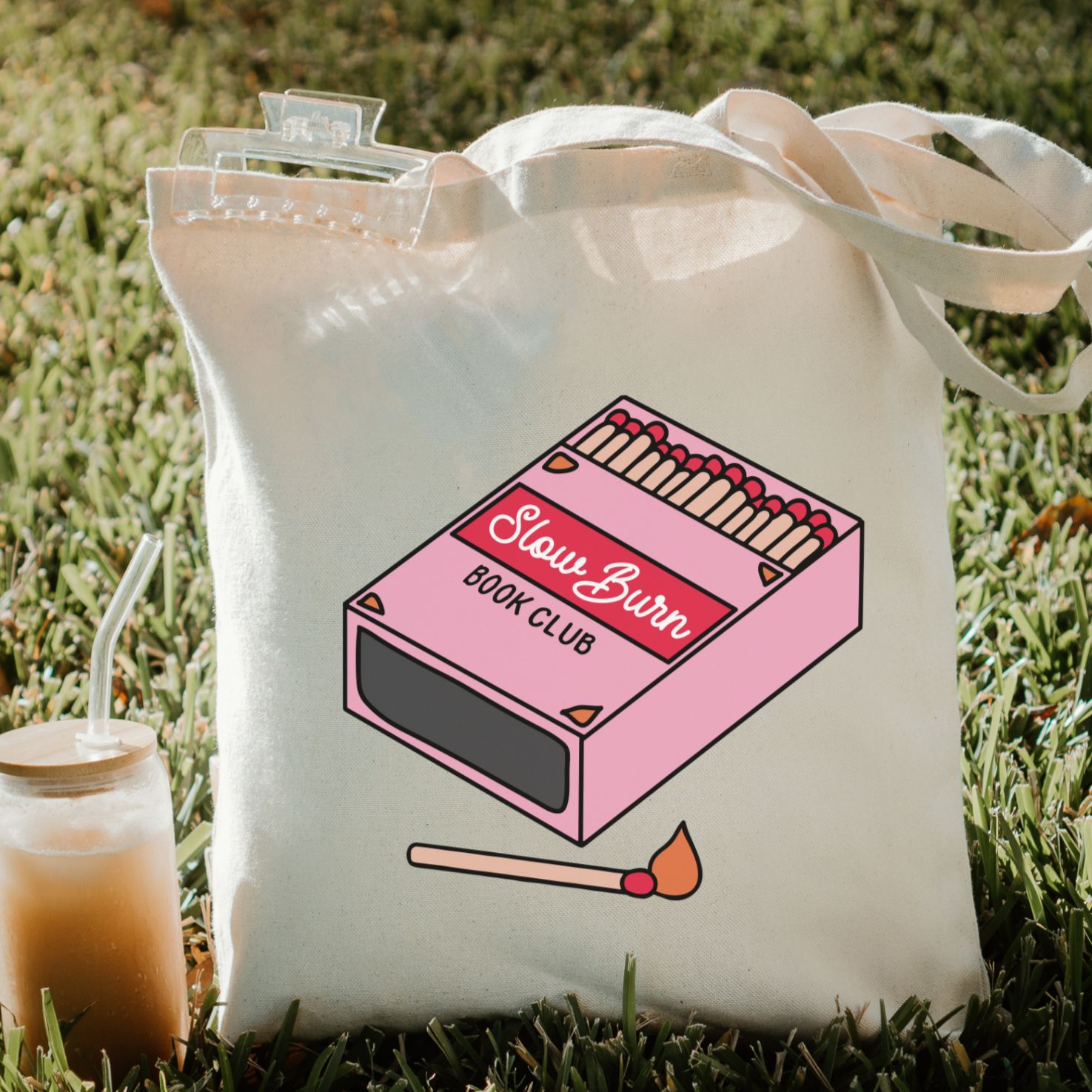 Bookish tote bag with a pink book club matchbox design on grass
