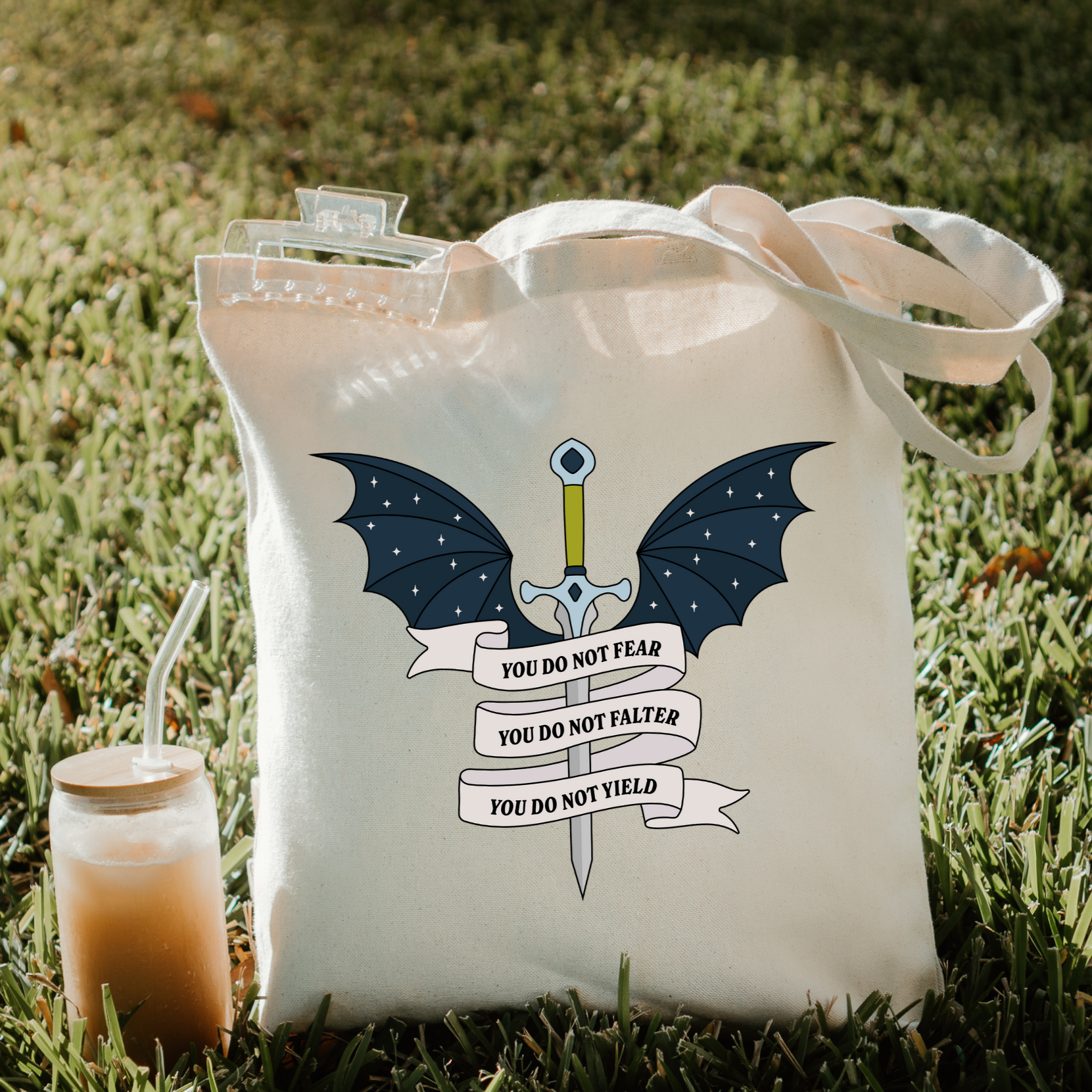 Bookish tote bag with a dragon design and text on grass