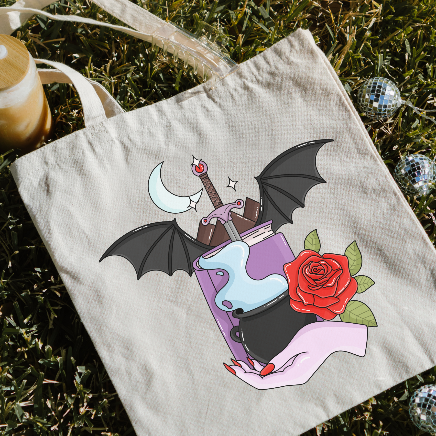 Bookish tote bag with a bat, rose, and potion design on grass