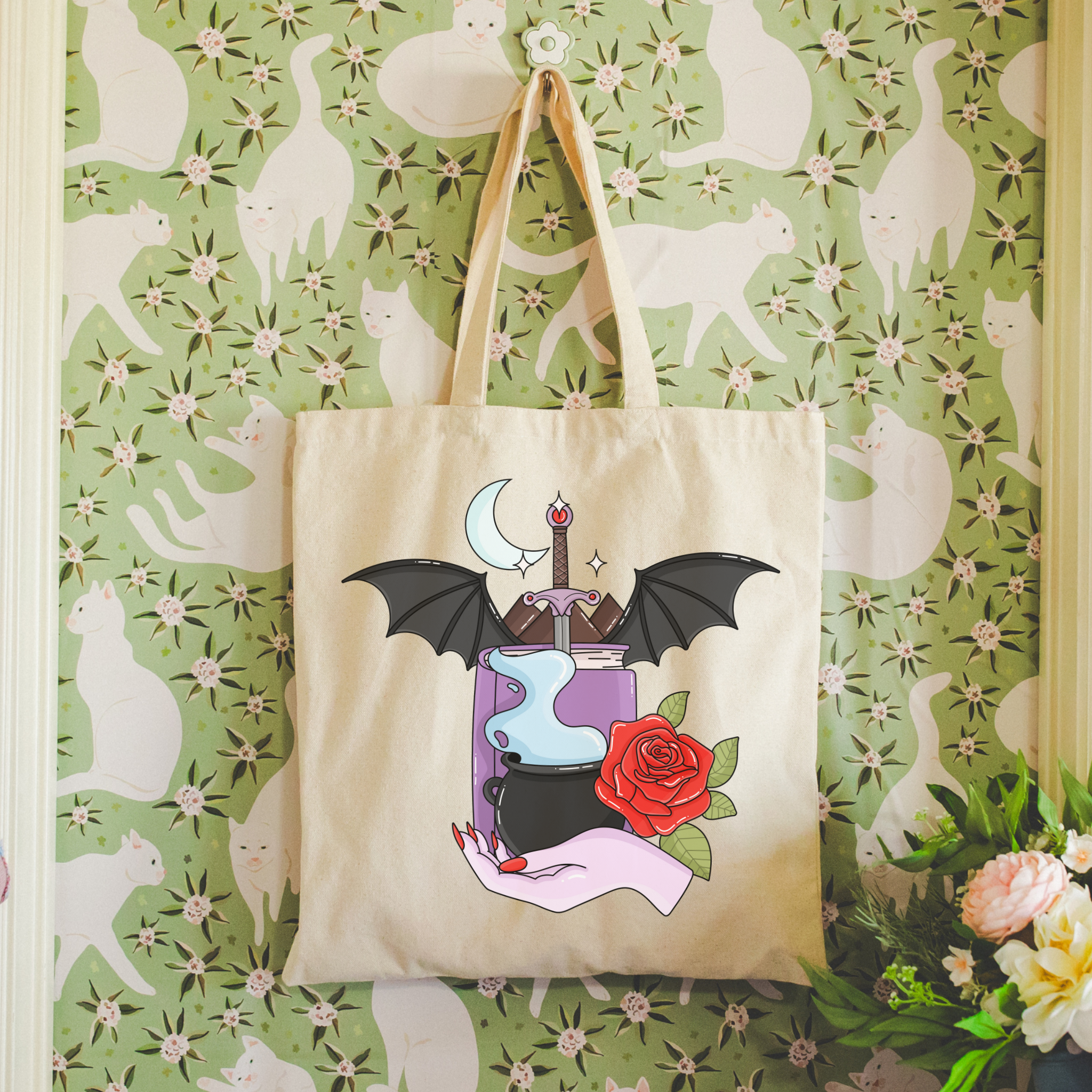 Bookish Tote bag with a design of a potion, bat, and rose hanging on a floral-patterned wall.