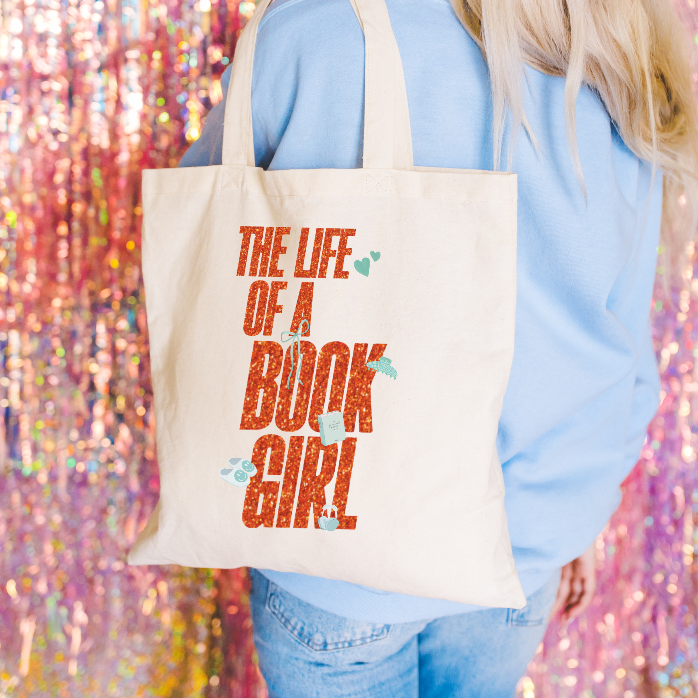 Tote bag with 'The Life of a Book Girl' text held by a person against a colorful, glittery background.