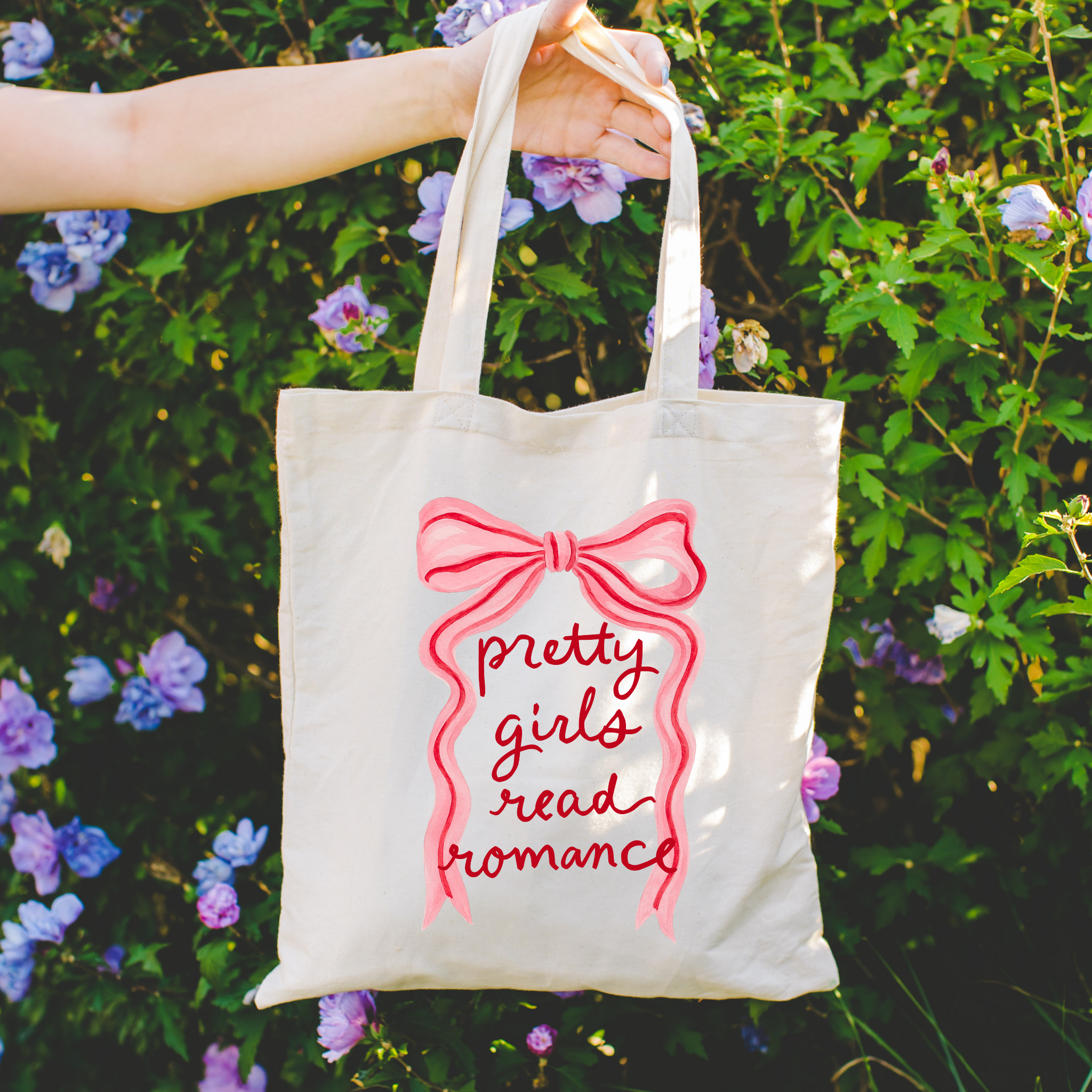 bookish Tote bag with 'pretty girls read romance' text and a bow design held in front of flowers.
