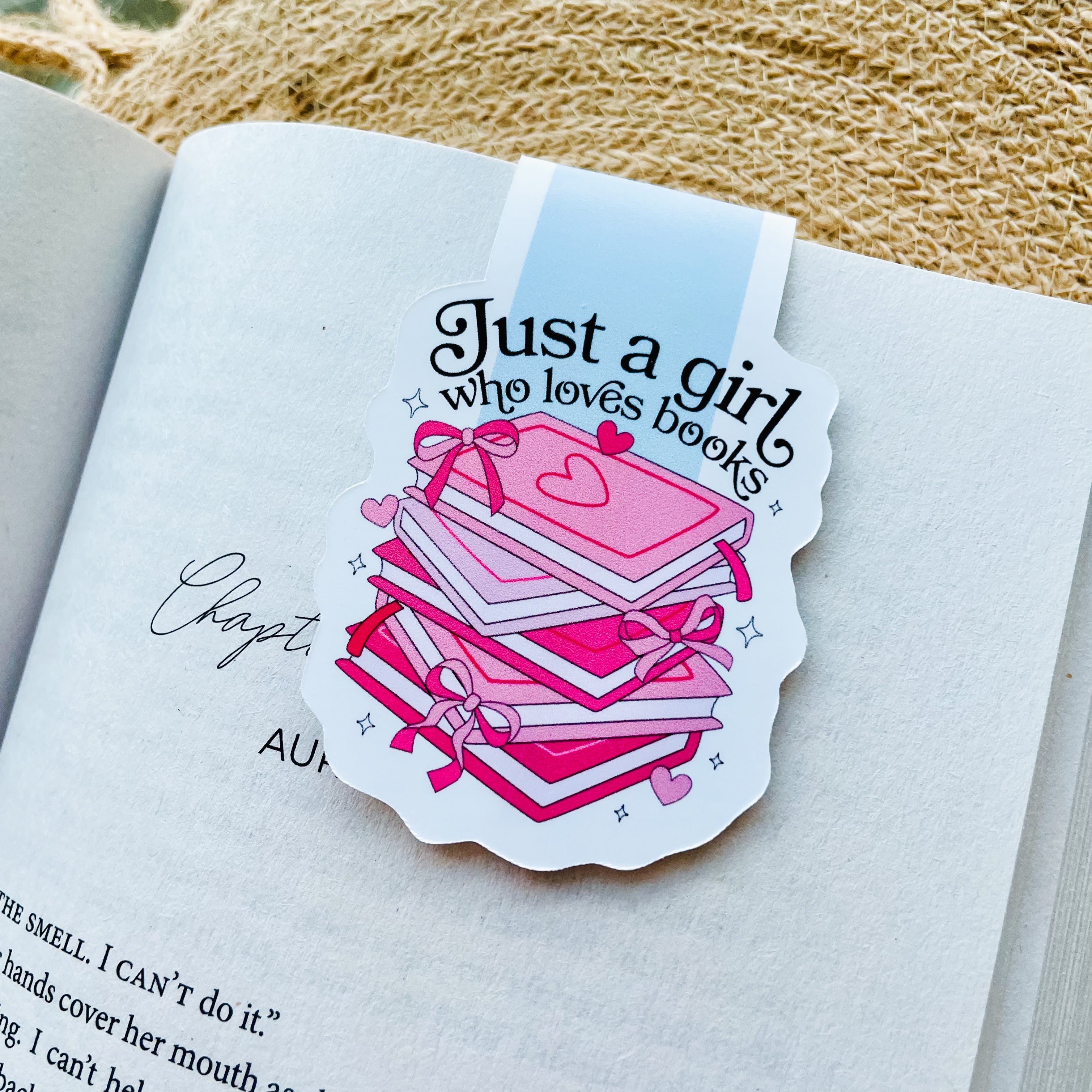 A magnetic bookmark with a pink and white design featuring the text 'Just a girl who loves books' and a graphic of stacked books.