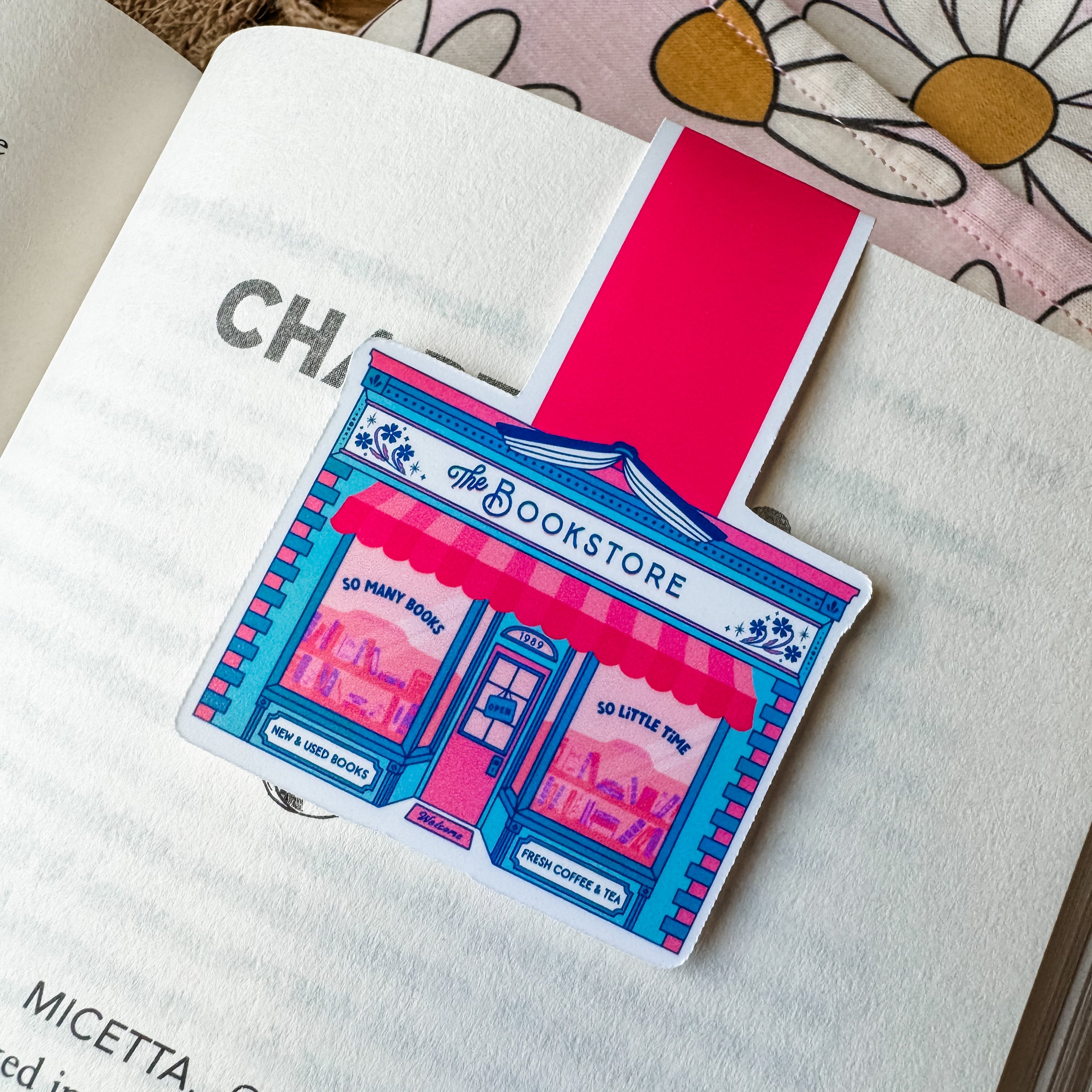 A magnetic bookmark with a pink bookstore design, placed on an open book.
