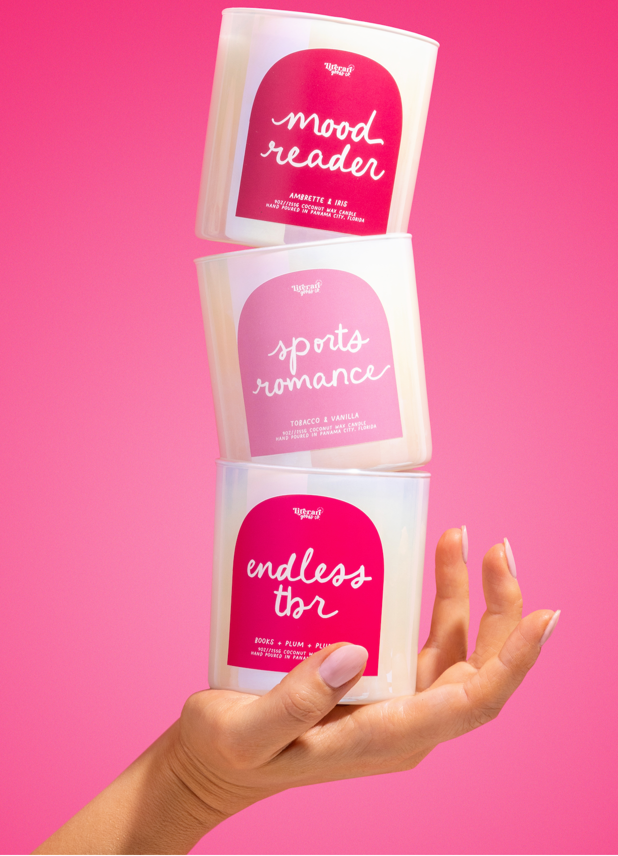 Three 'mood reader' bookish candles held by a hand against a pink background
