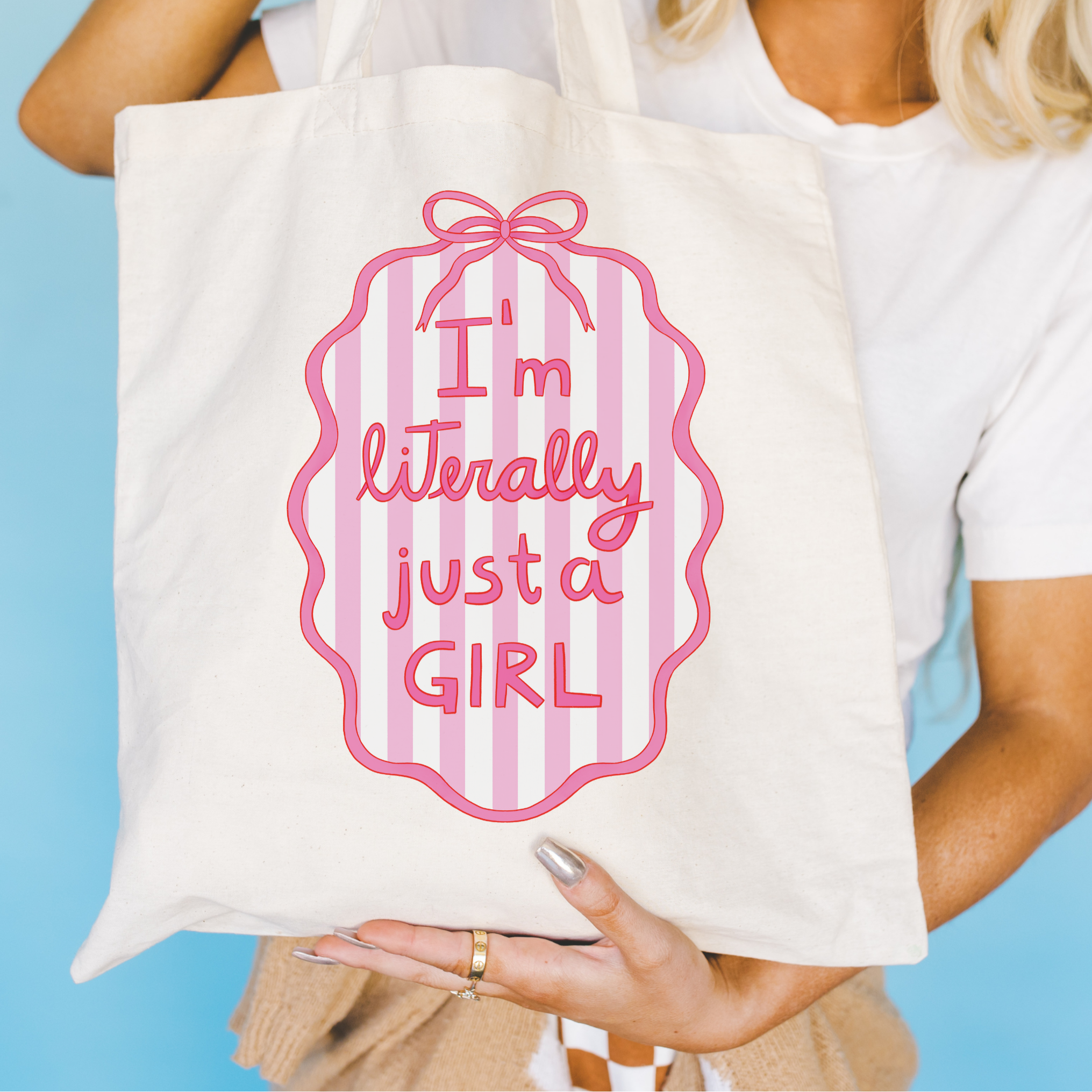 Tote bag with pink text, "I'm Literally Just a Girl" and design held by a person against a blue background