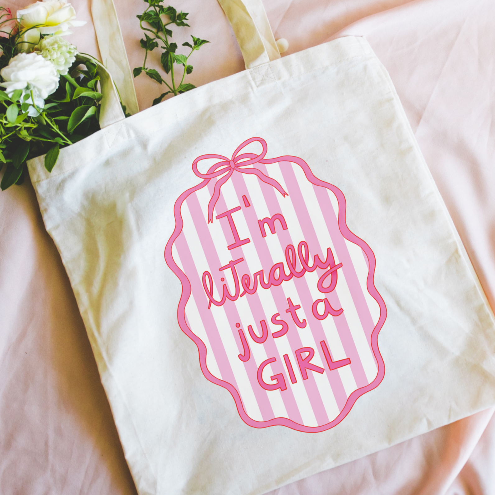Tote bag with 'I'm literally just a girl' text on a pink surface with flowers.
