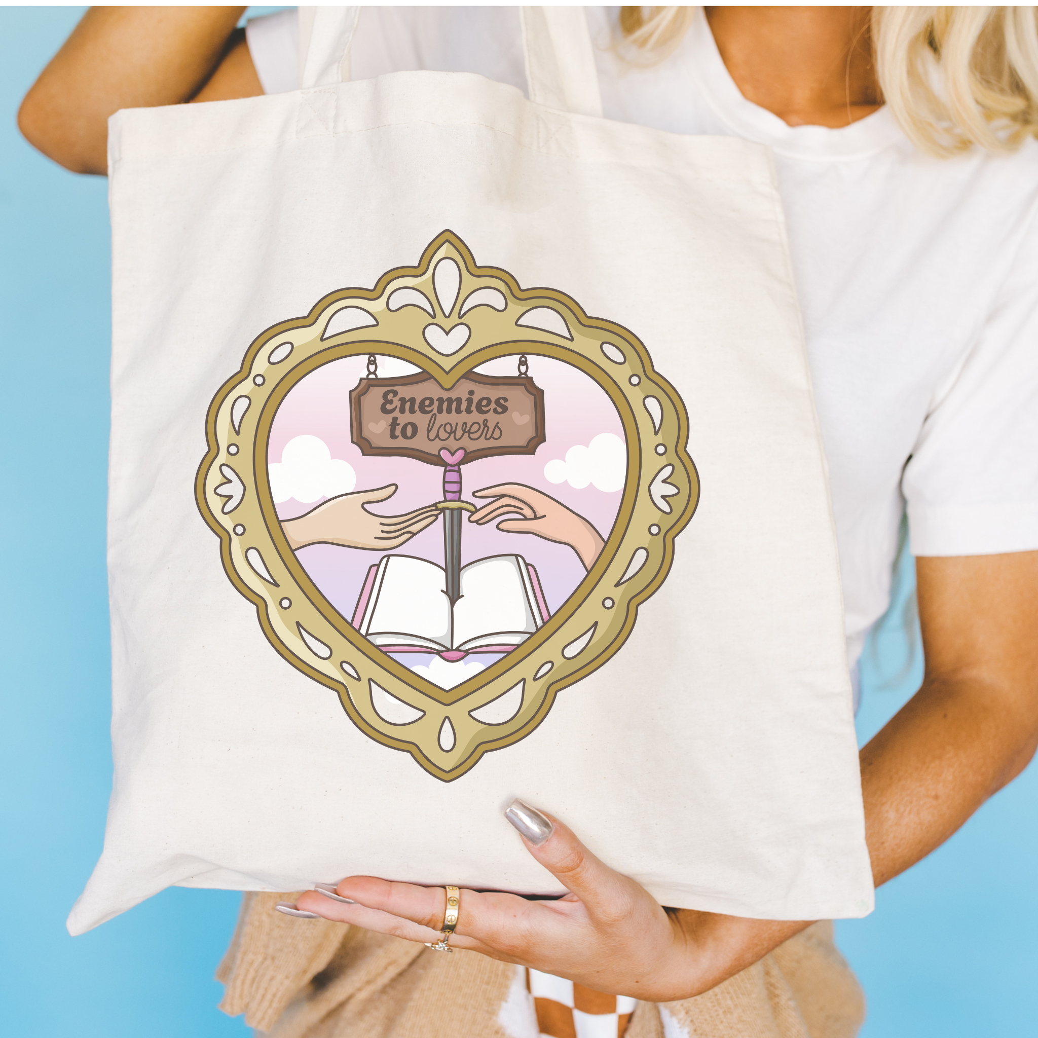 Tote bag with decorative design featuring hands, an open book, and "Enemies to Lovers" on a blue background