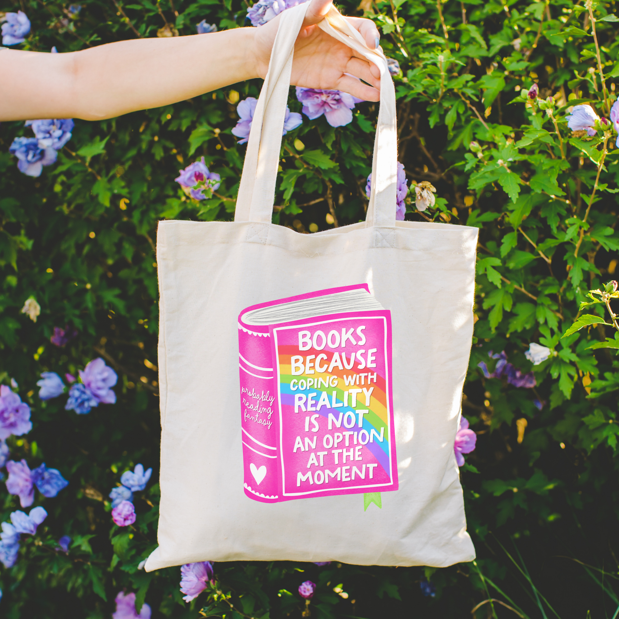 Person holding a bookish tote bag with a colorful book design and text.