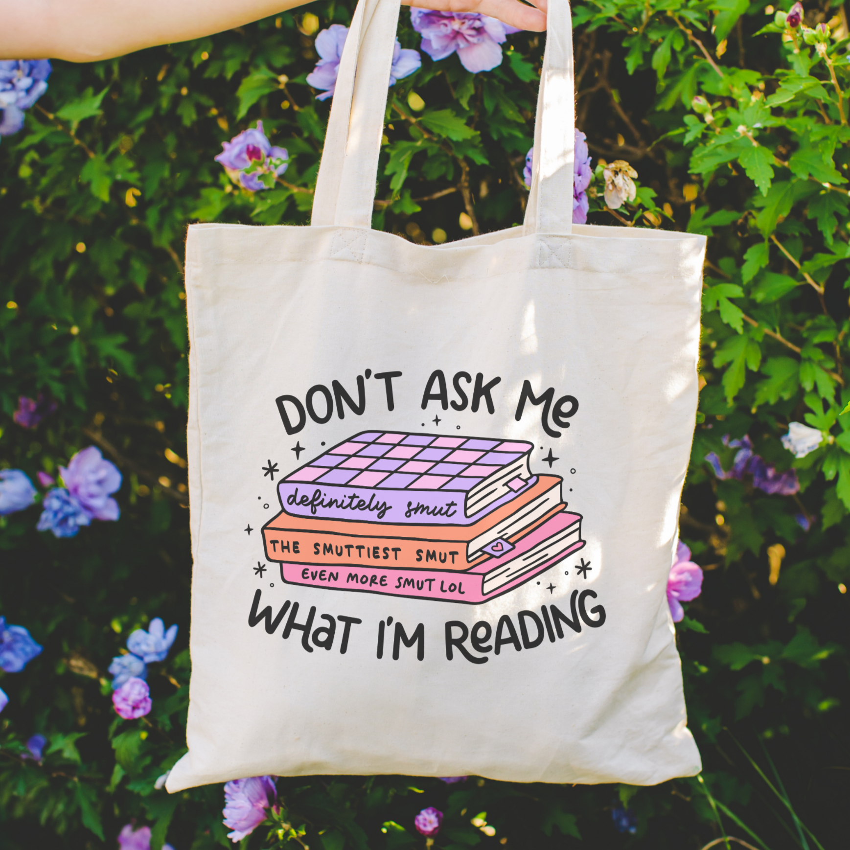 Tote bag with humorous book-themed text held in front of a floral background