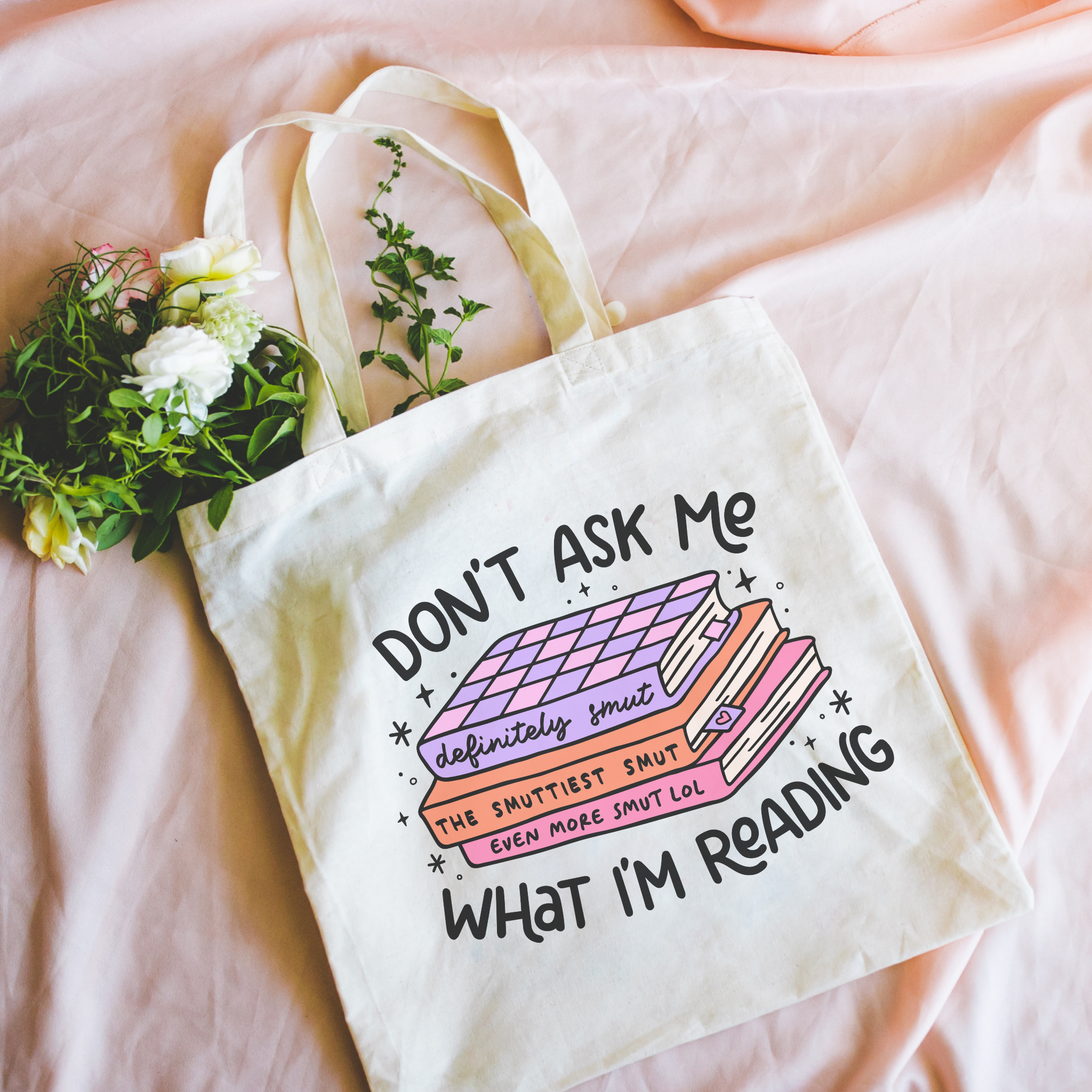 Bookish tote bag with humorous text design on a pink surface with flowers.