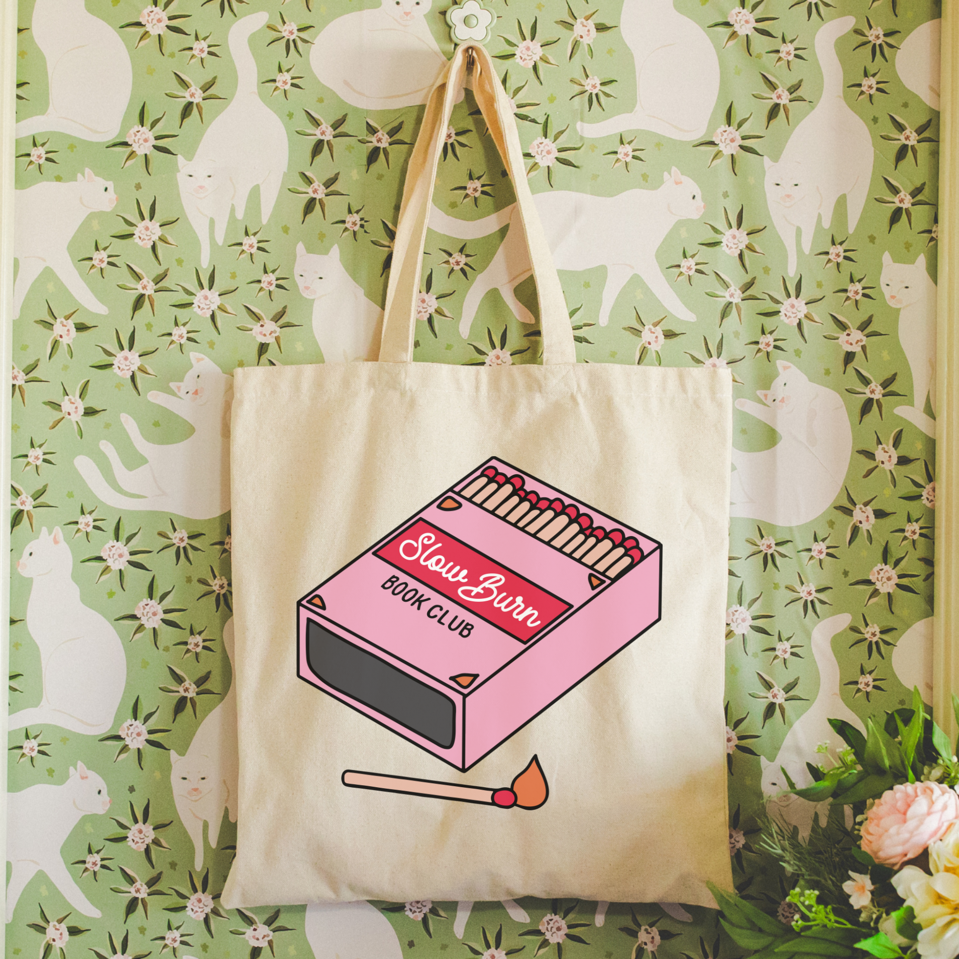 Bookish trope Tote bag with matchbox design hanging on a floral-patterned wall