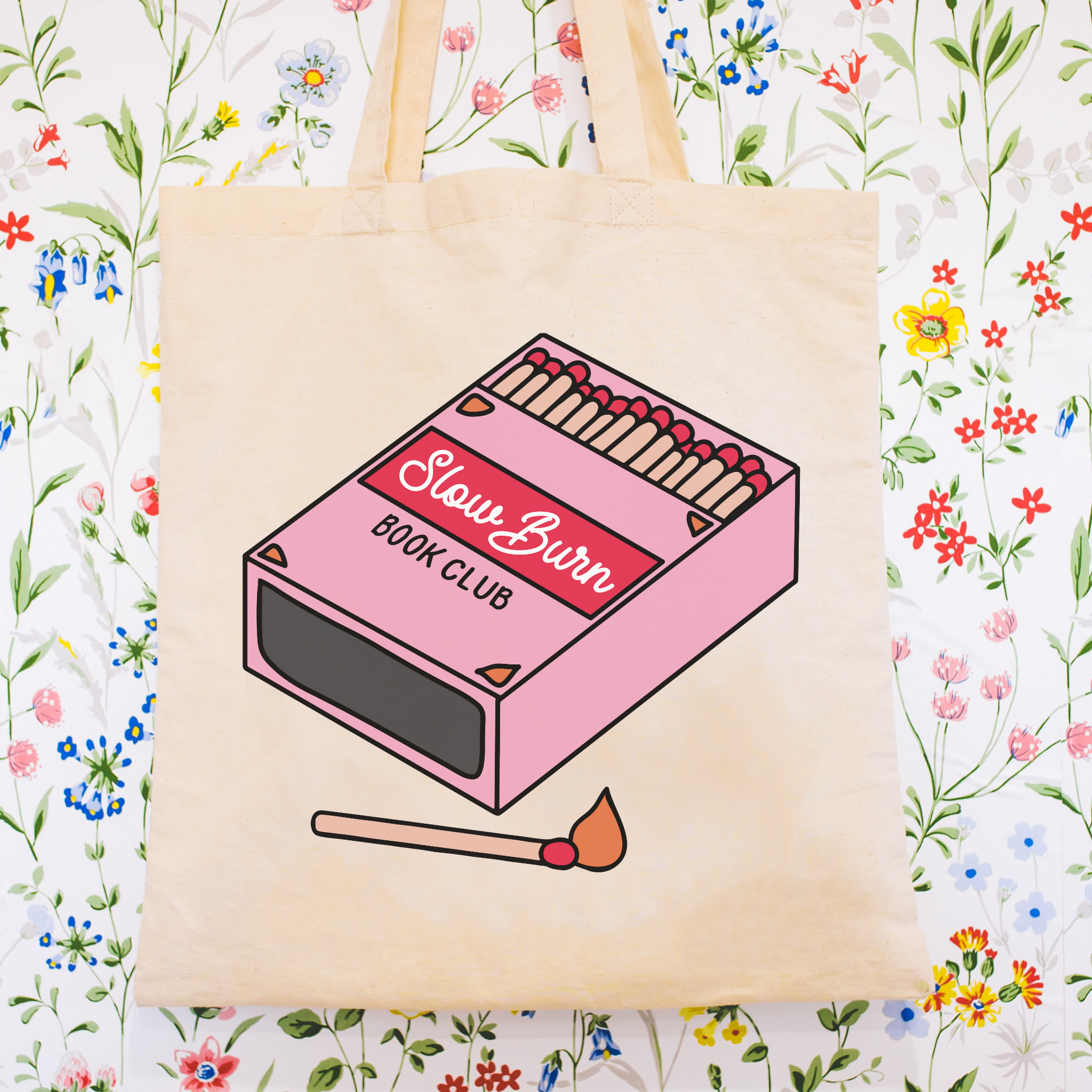 Tote bag with a pink matchbox design and 'Slow Burn Book Club' text on a floral background