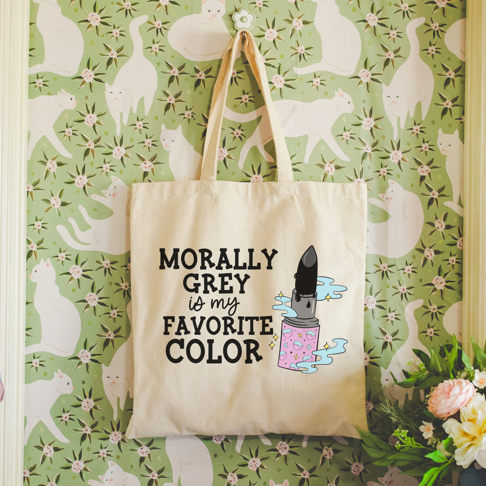 bookish tote bag with 'Morally Grey is my Favorite Color' text and graphic on a floral cat-patterned wall.