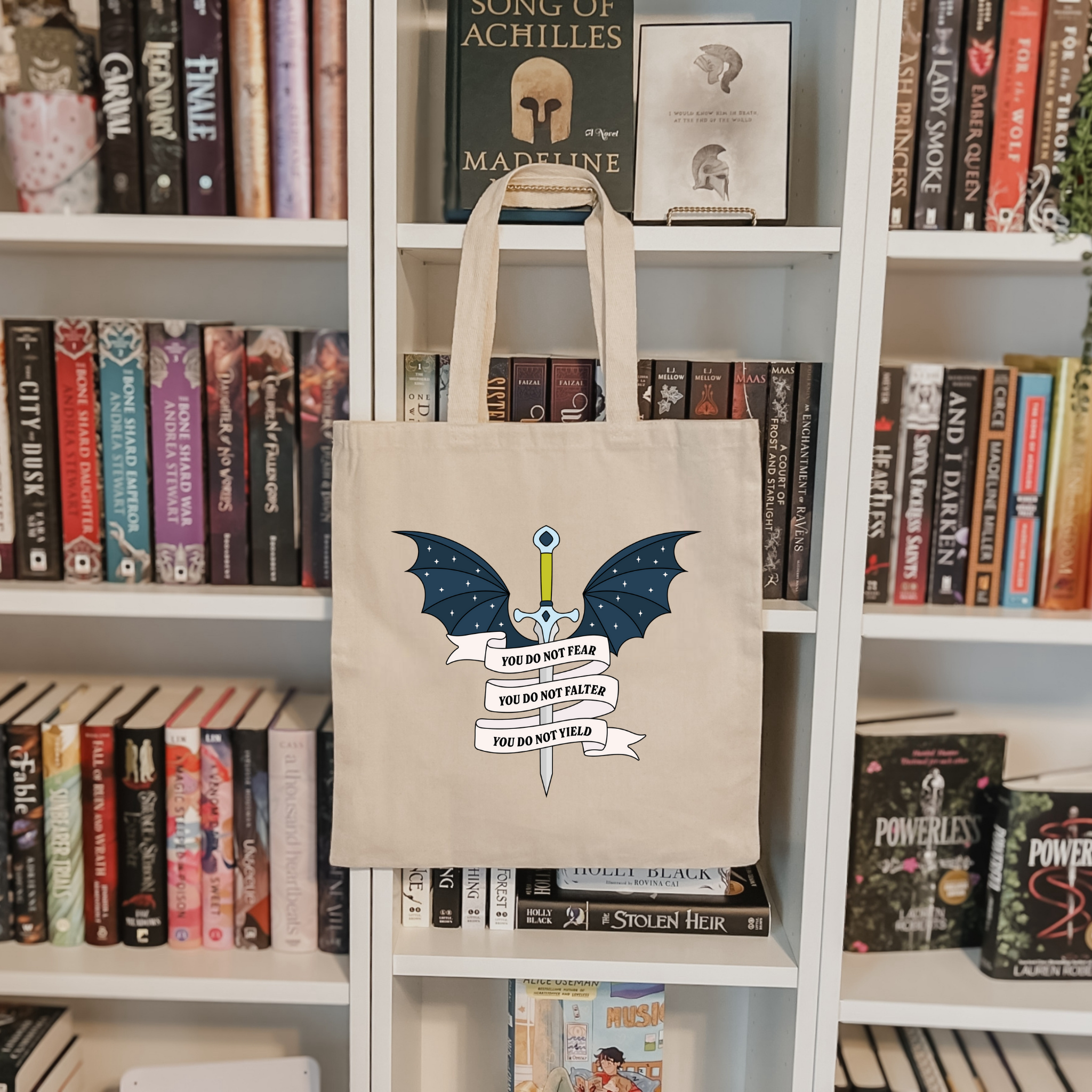 Bookish tote bag with bat design and text on a bookshelf background