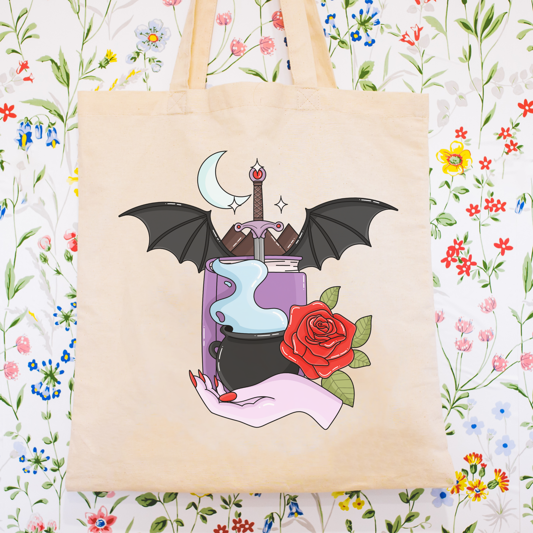 Bookish Tote bag with a design of a hand holding a potion, bat, and rose on a floral background