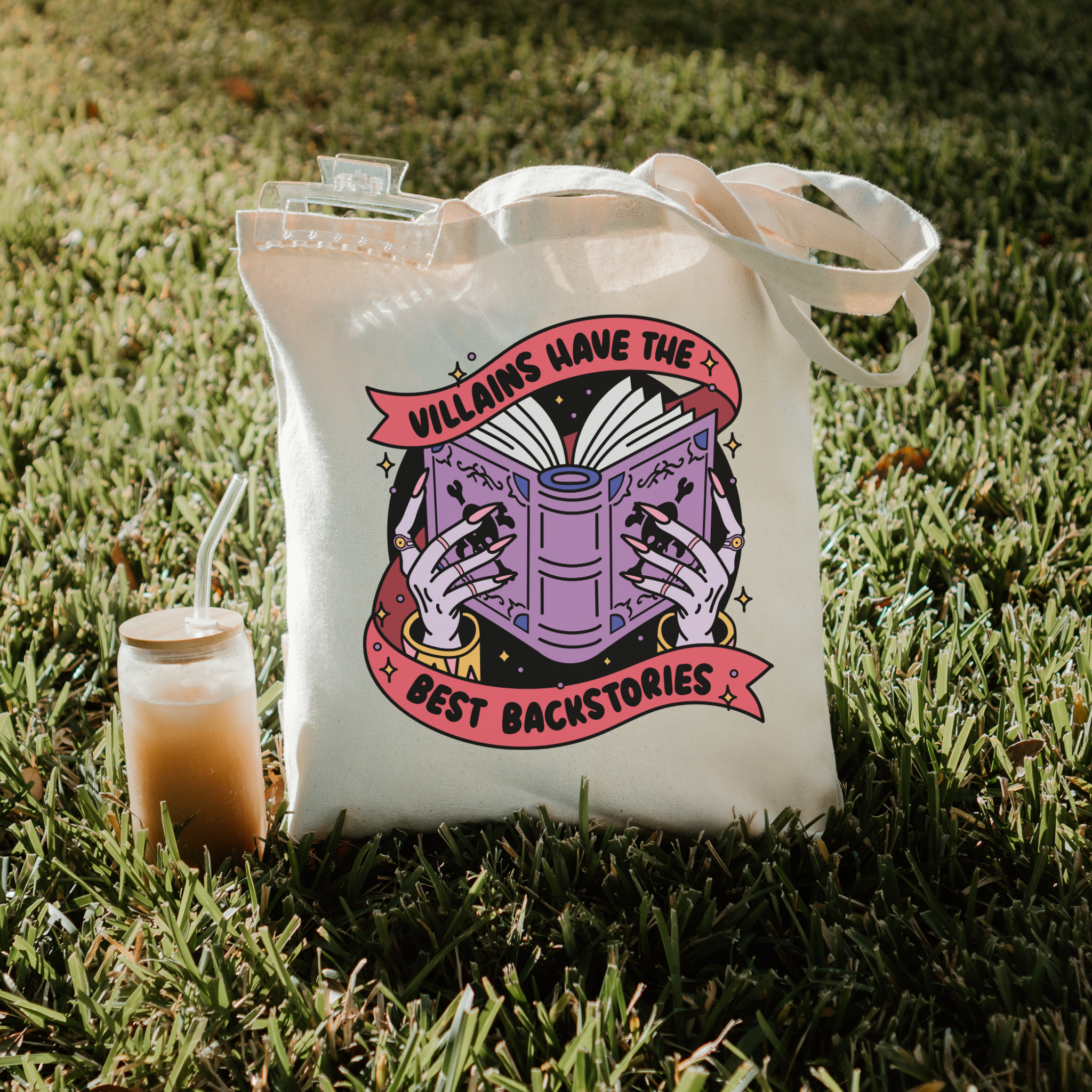 bookish tote bag with graphic design on grass next to a drink