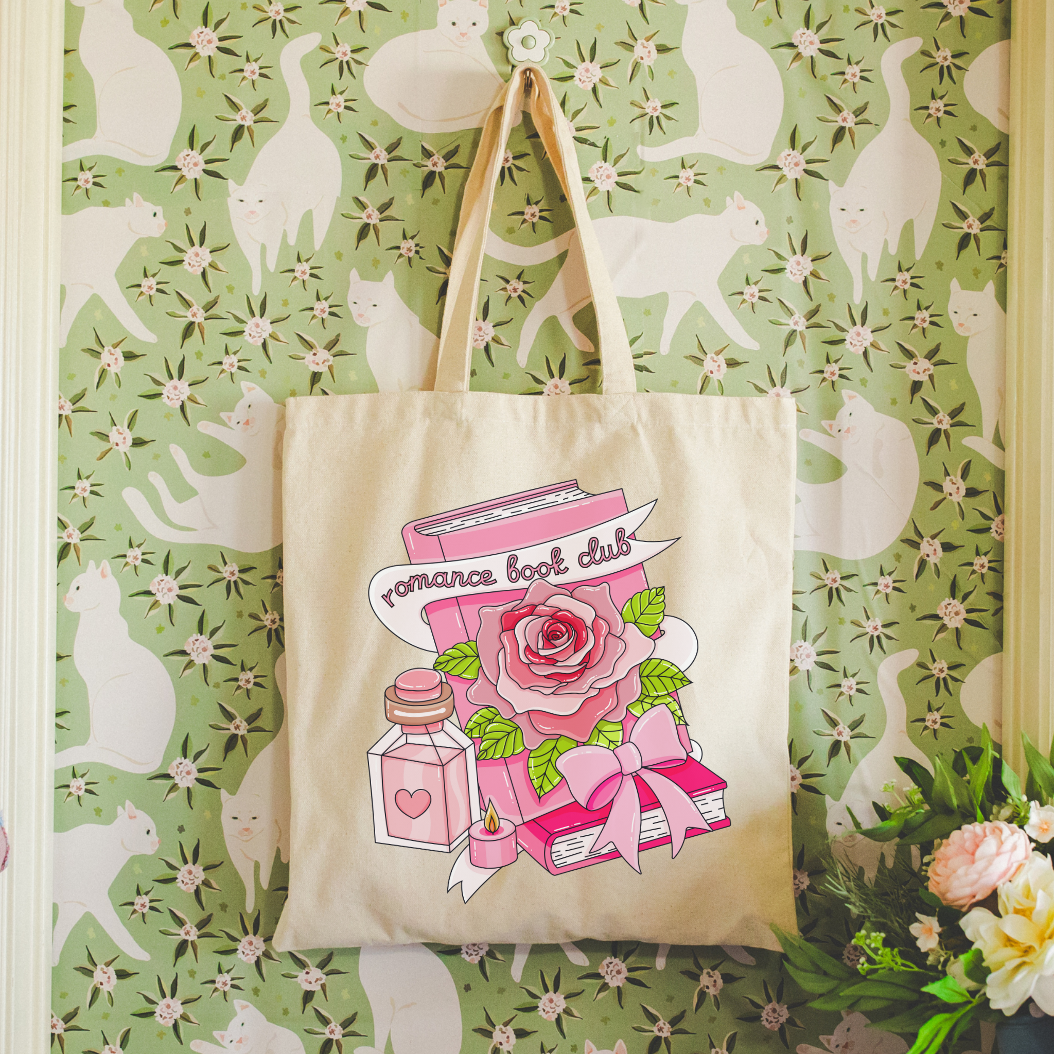 Tote bag with 'romance book club' design hanging on a floral-patterned wall.