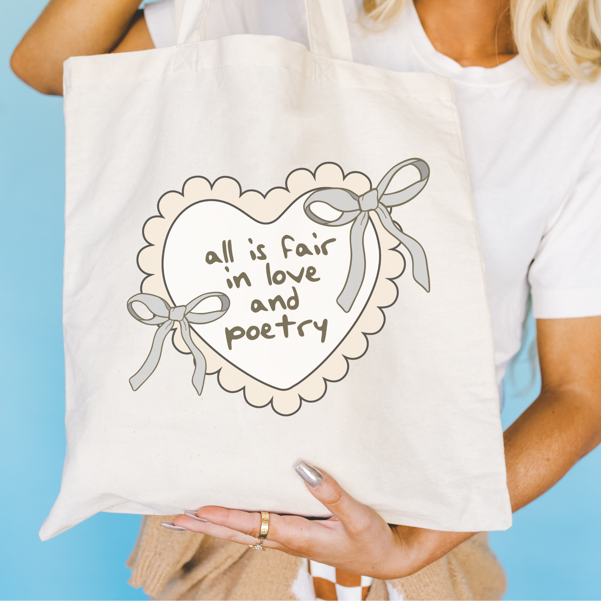 Person holding a Bookish tote bag with a heart design and text against a blue background