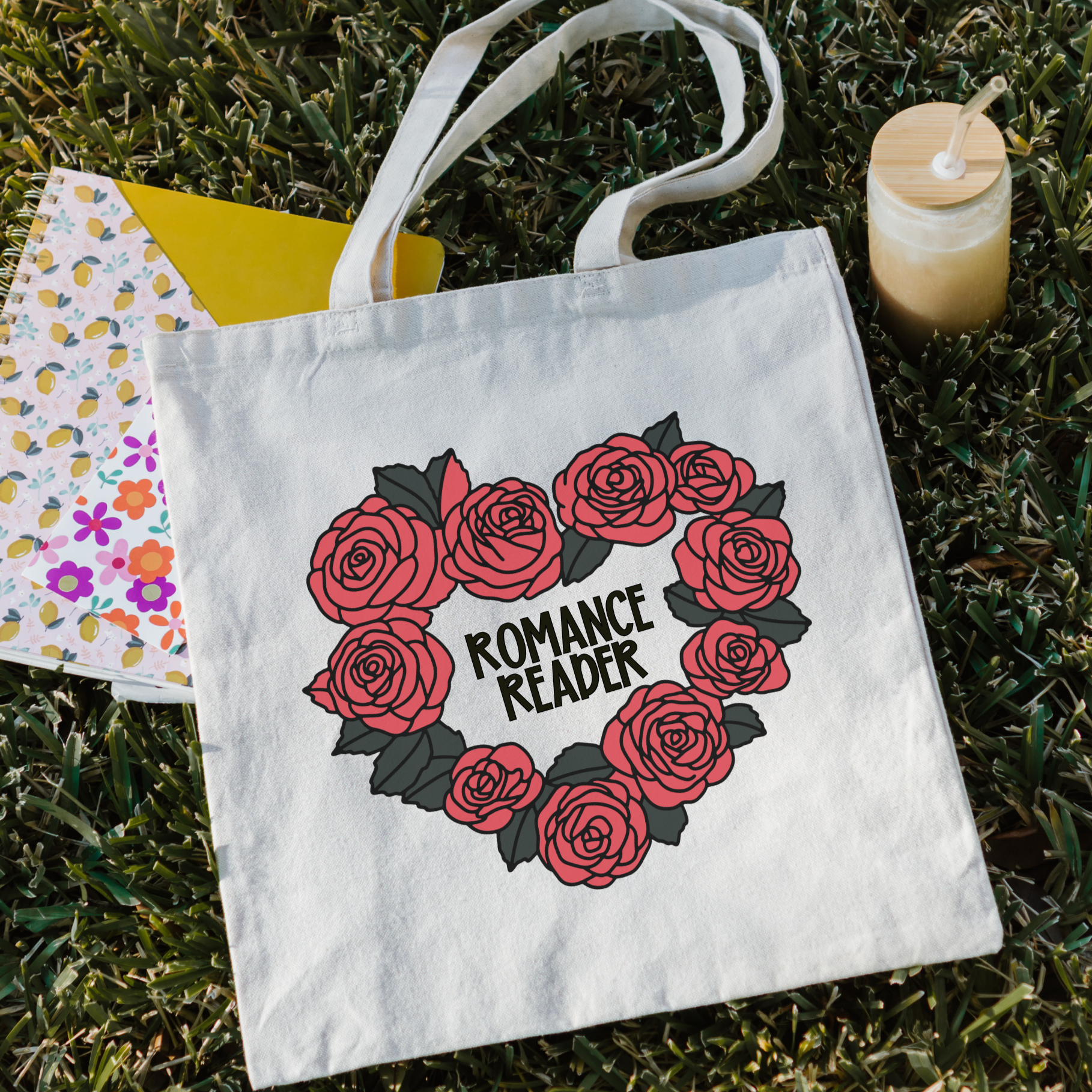 bookish Tote bag with 'Romance Reader' design on grass with a drink and notebook.