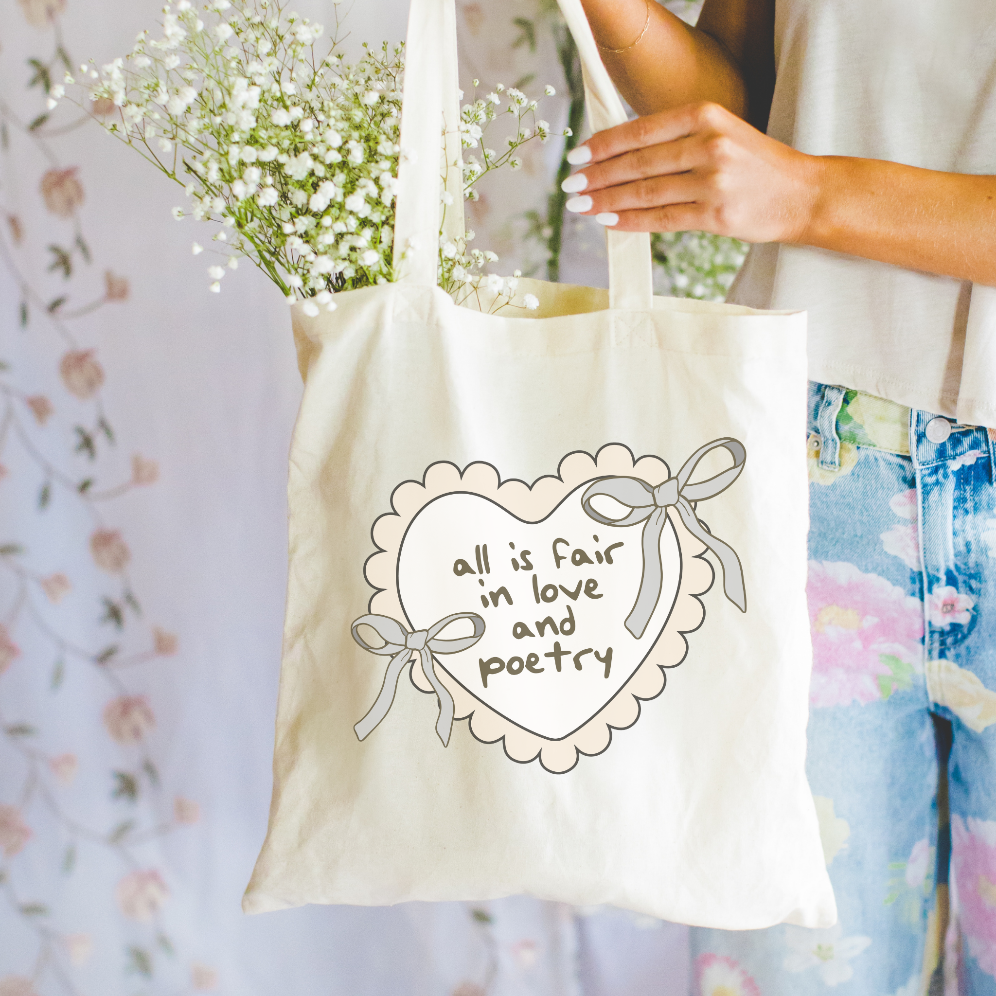 Bookish Tote bag with 'all is fair in love and poetry' text and floral arrangement, held by a person.