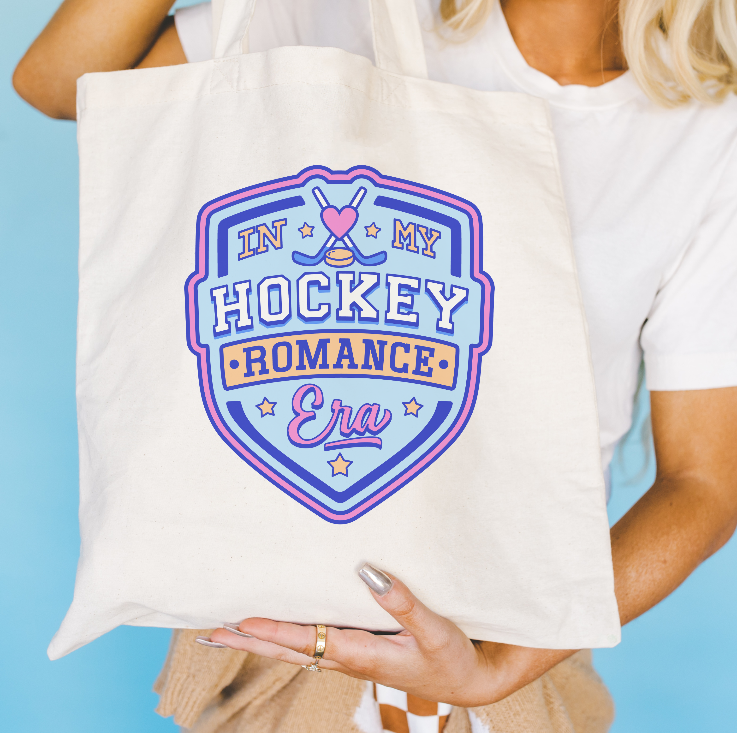 Person holding a tote bag with 'In My Hockey Romance Era' design with a shield and hockey pucks