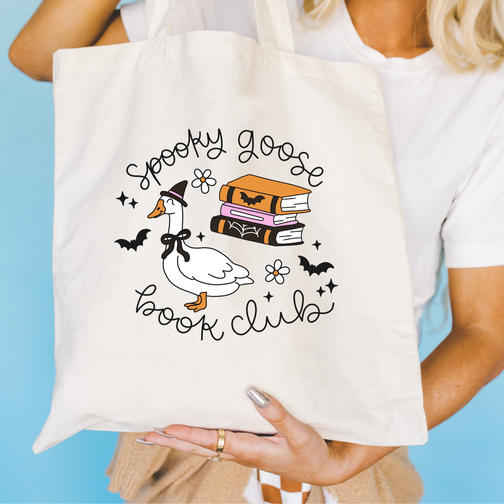 Tote bag with 'Spooky Goose Book Club' design held by a person against a blue background