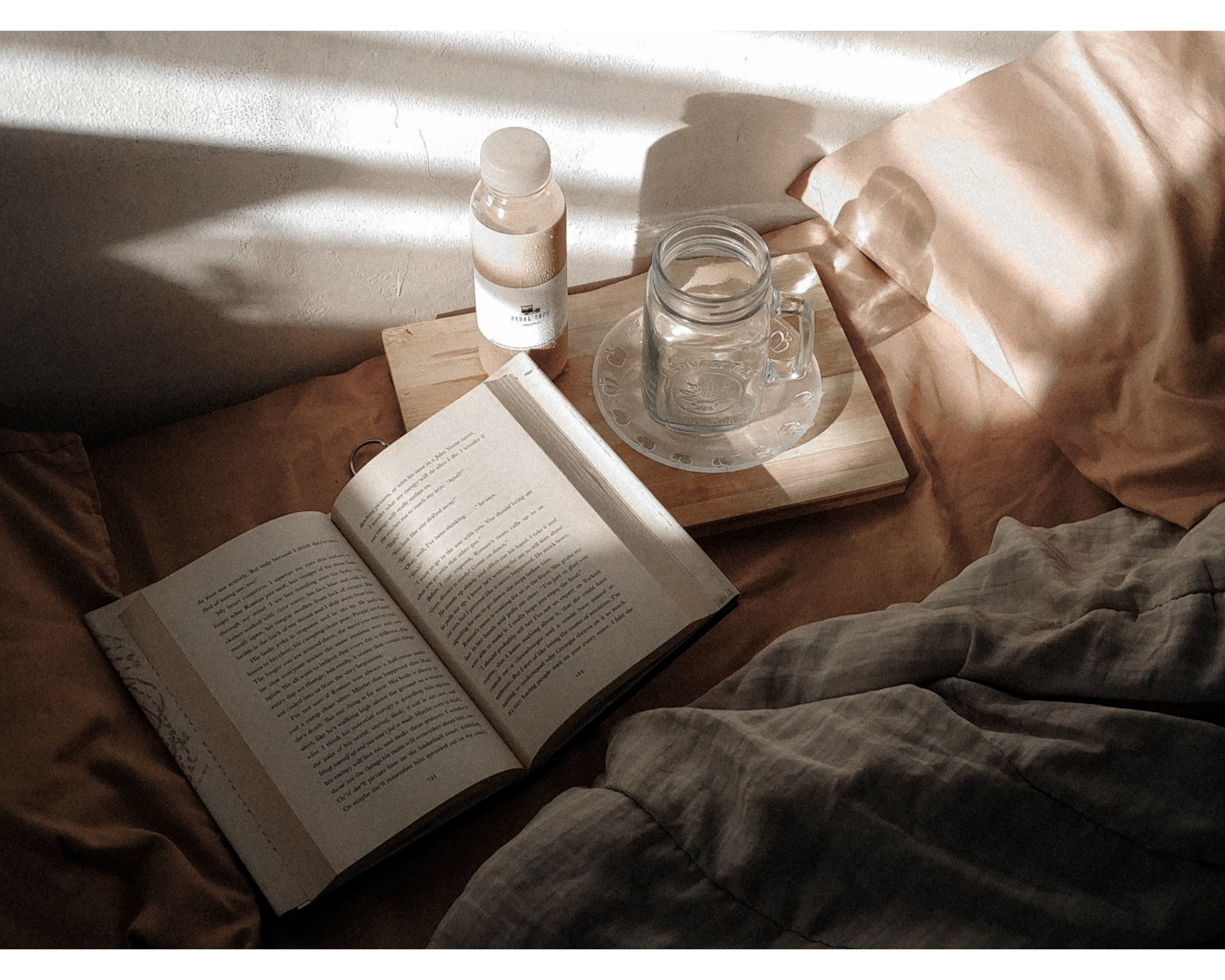 Open book on a wooden surface with a bottle and jar, soft natural light filtering through.