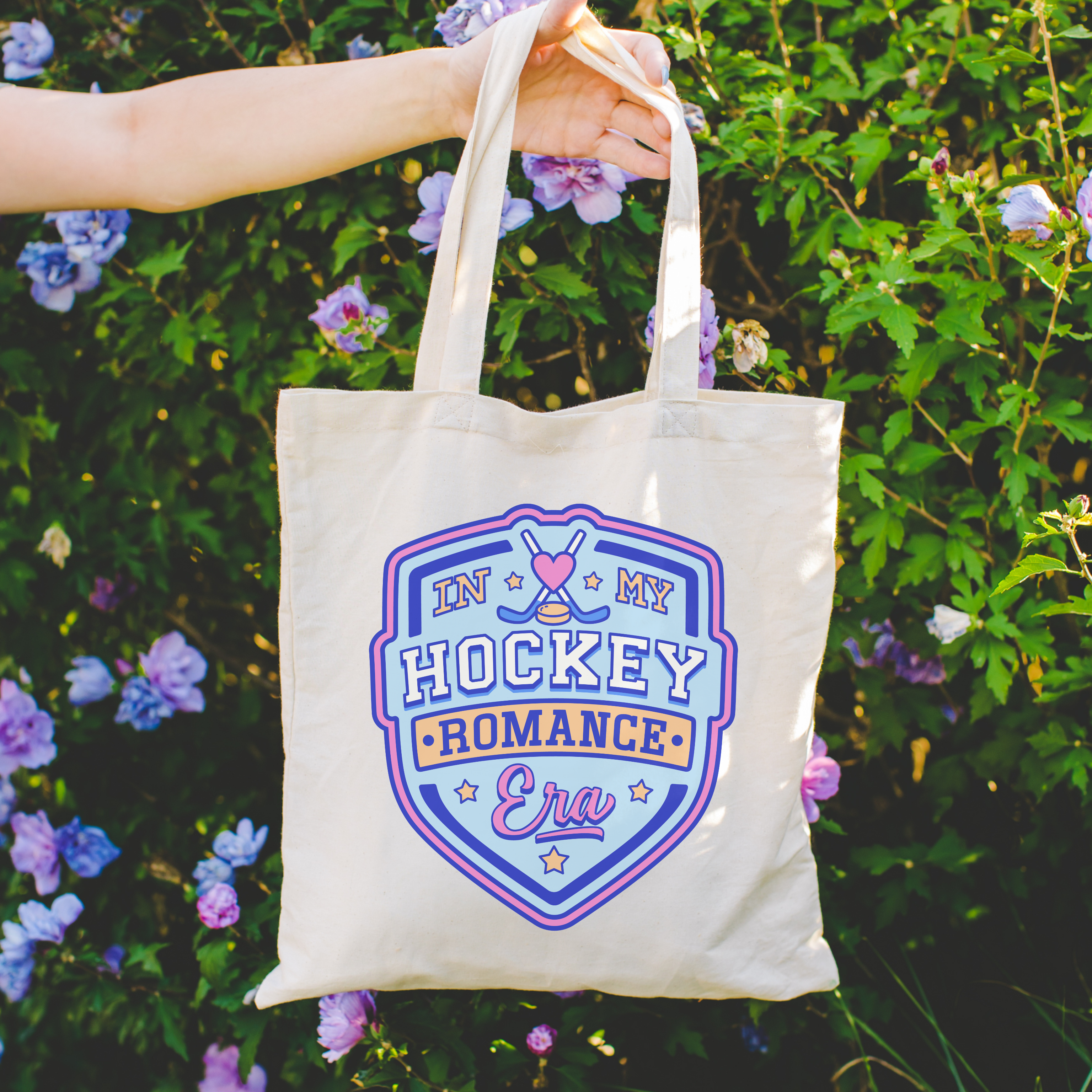 Tote bag with 'In My Hockey Romance Era' design held in front of a floral background