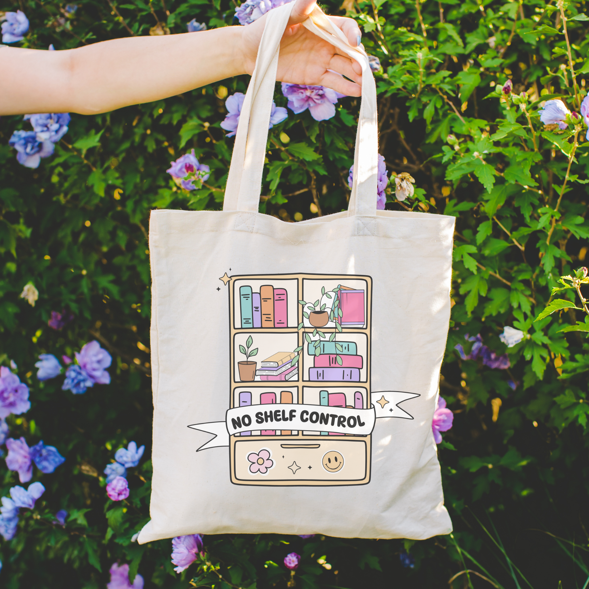 Bookish Tote bag with a bookshelf design and 'No Shelf Control' text held in front of a floral background