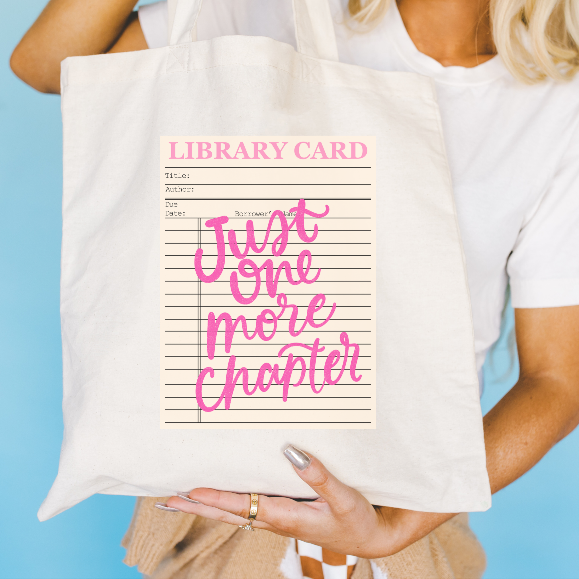 Bookish Tote bag with 'Library Card Just One More Chapter' design held by a person against a blue background