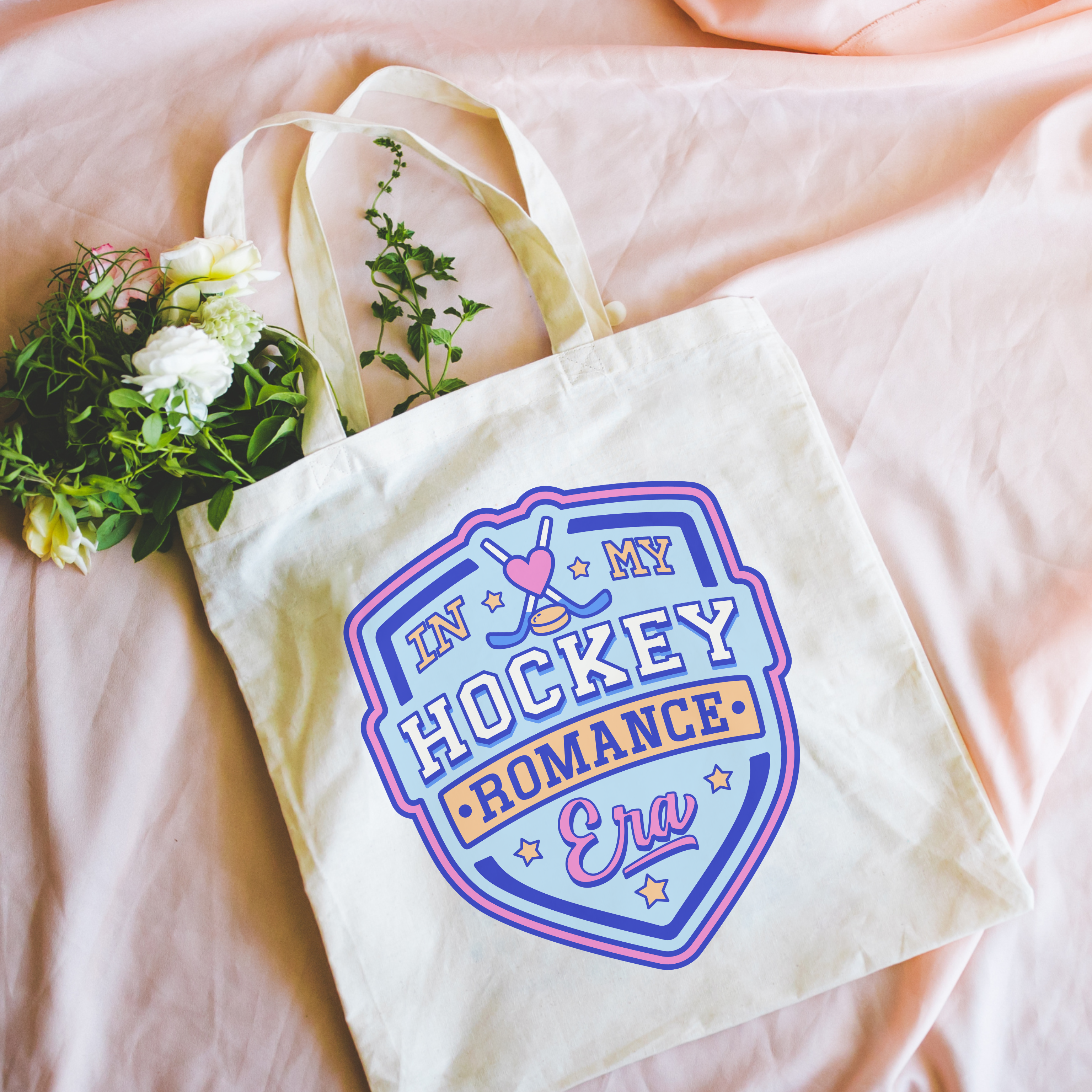 Tote bag with 'In My Hockey Romance Era' design on a pink surface with flowers.