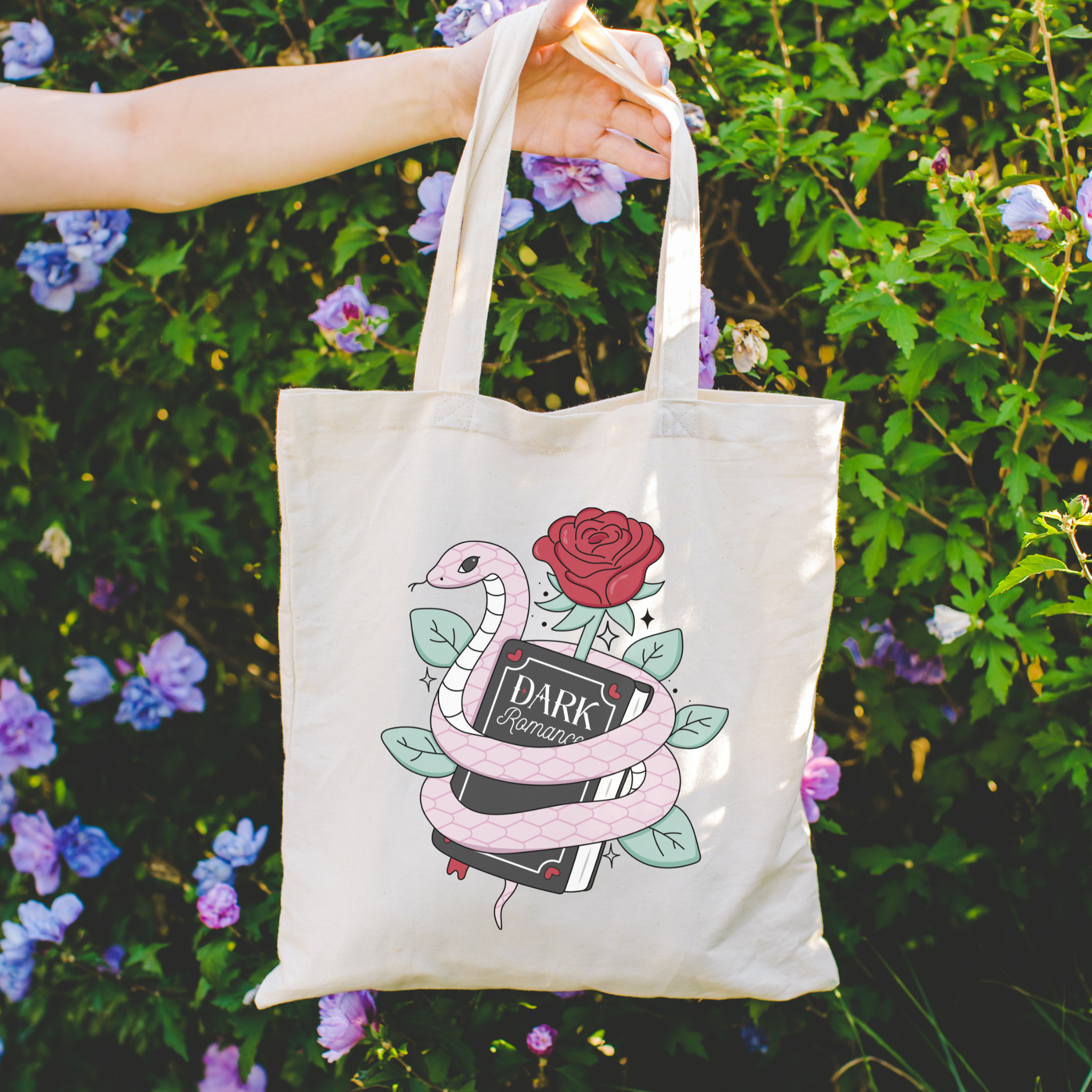 Dark Romance Tote bag with snake and rose design held in front of a floral background