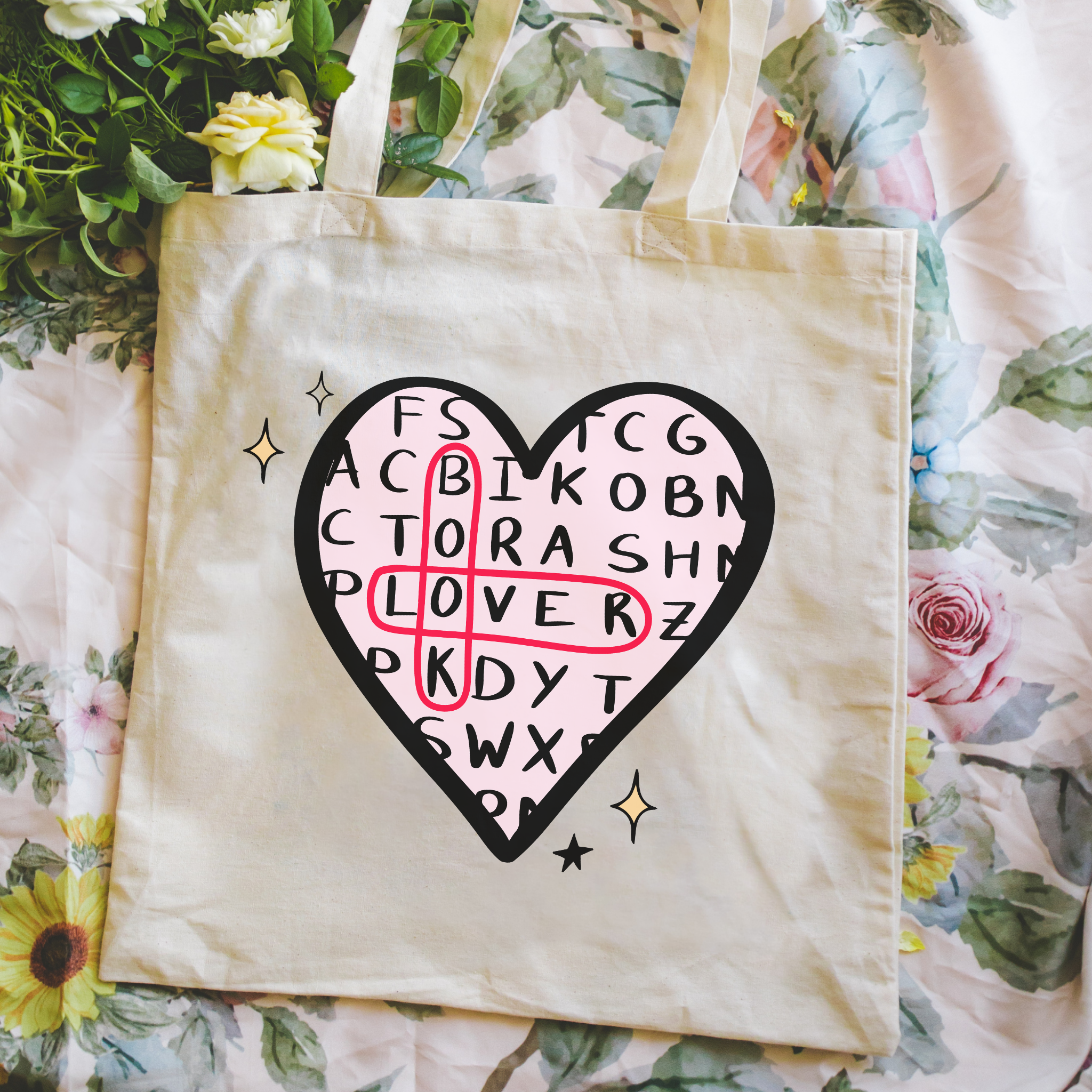 Bookish tote bag with a heart-shaped design on a pink surface with flowers. 