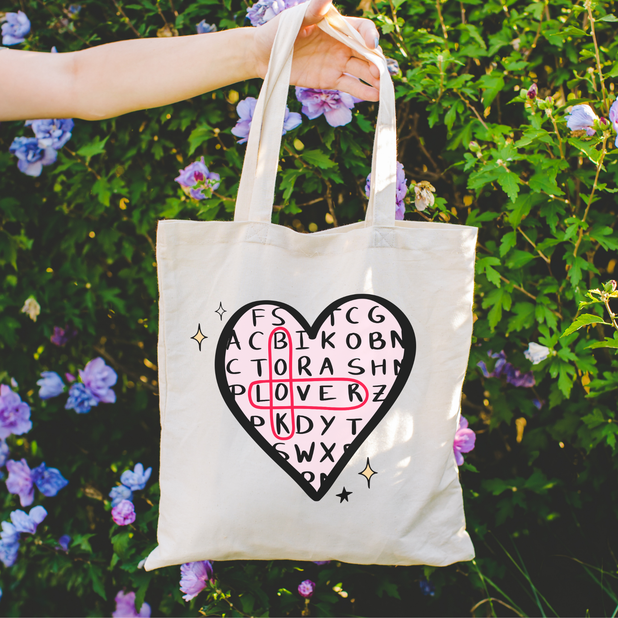 bookish tote bag with a heart design and text held in front of a floral background