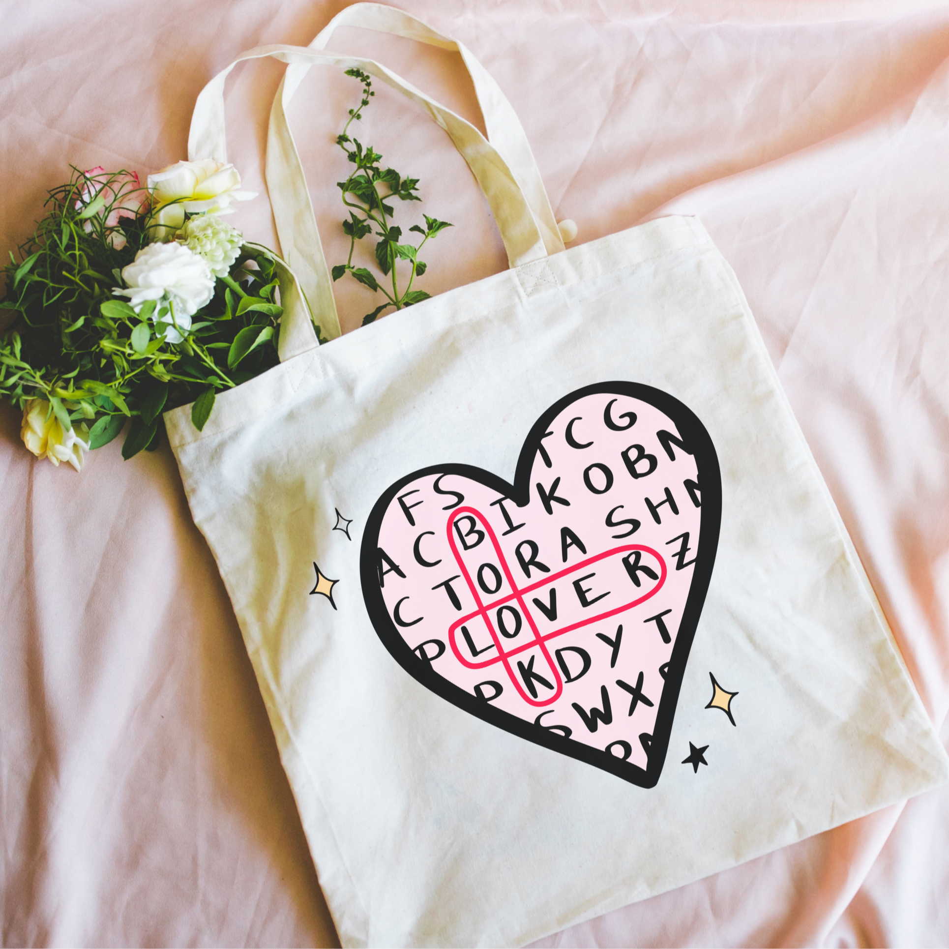 Bookish tote bag with a heart-shaped design on a pink surface with flowers.