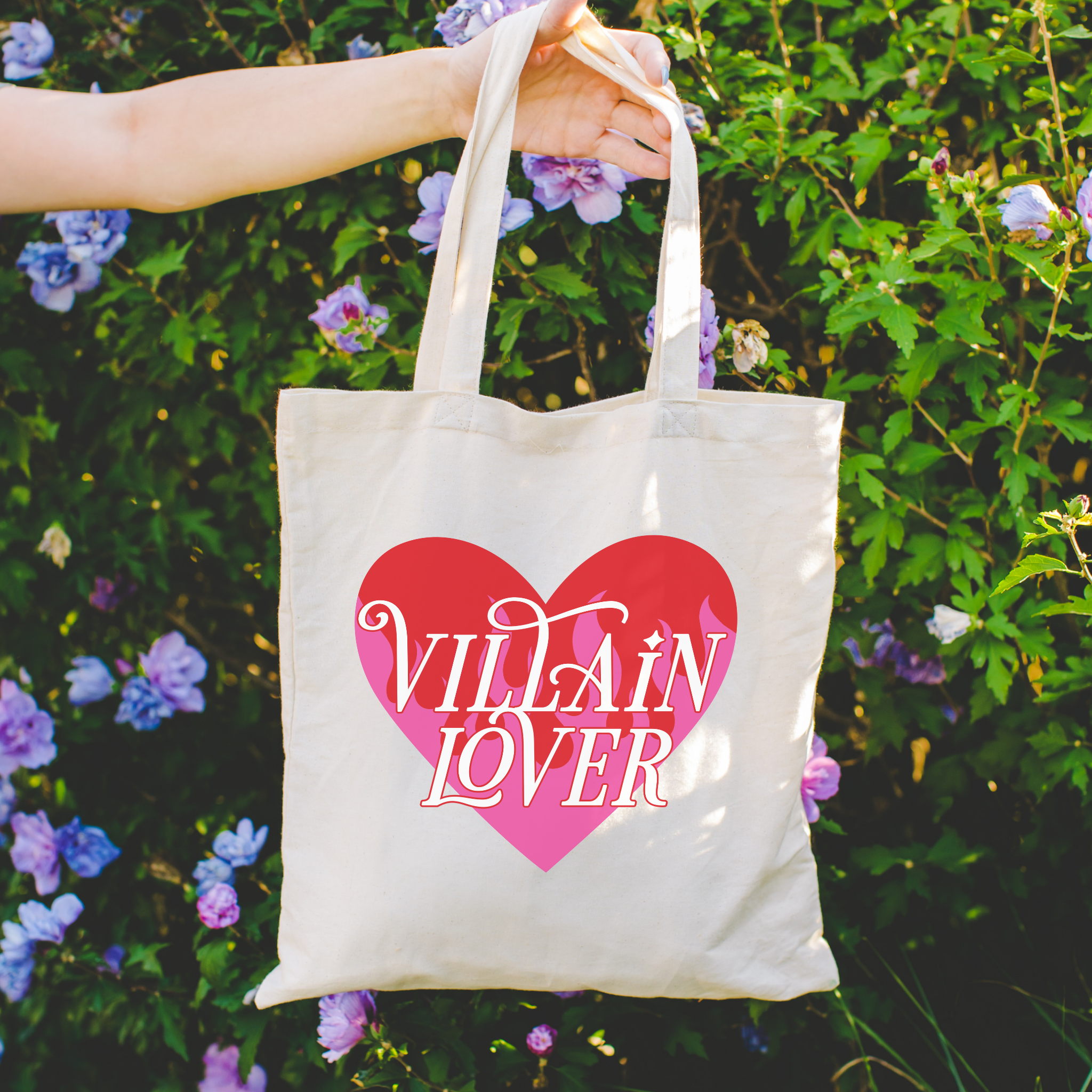 Bookish Tote bag with 'VILLAIN LOVER' design held in front of a floral background