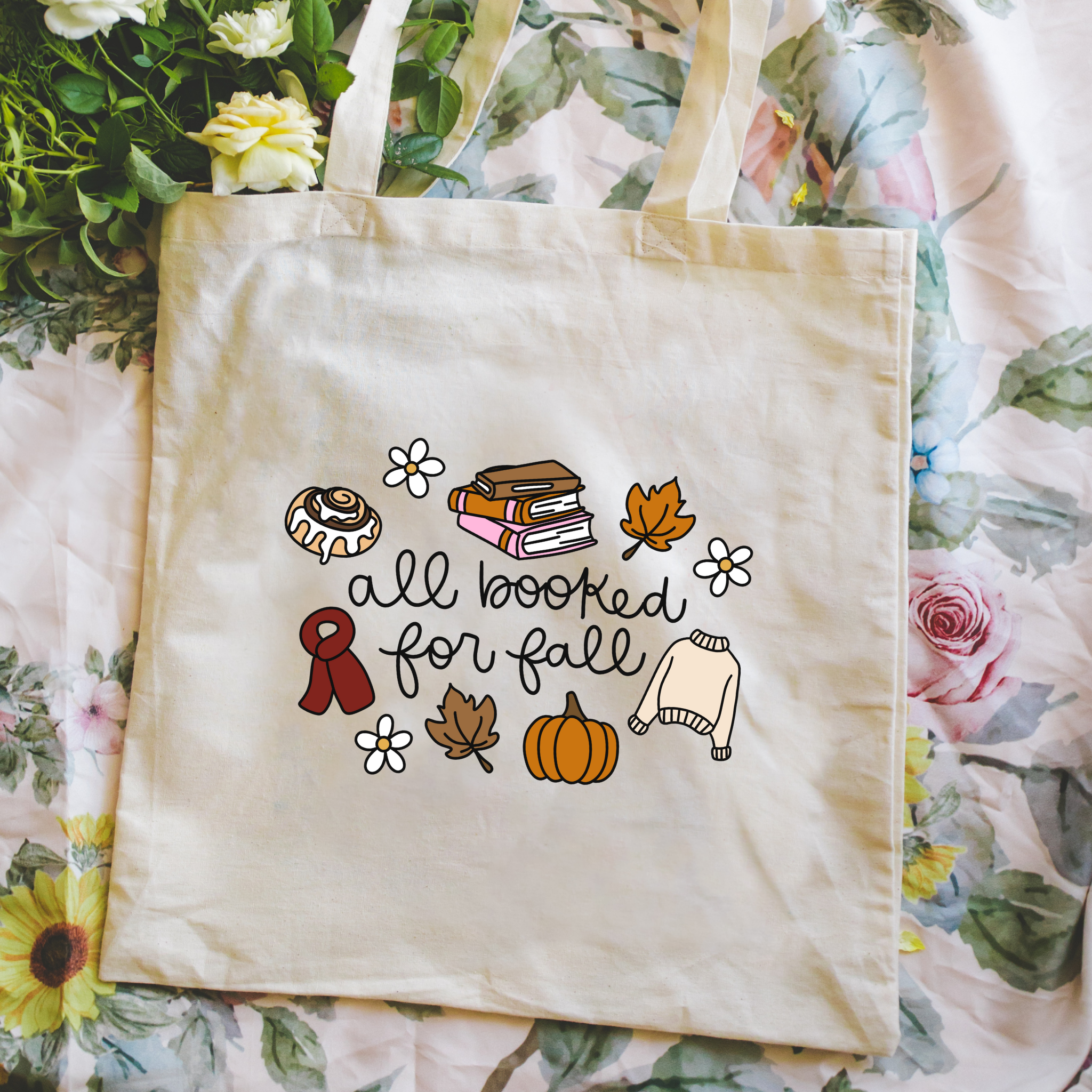 Bookish tote bag with autumn-themed illustrations and text on a floral background with text "all booked for fall"