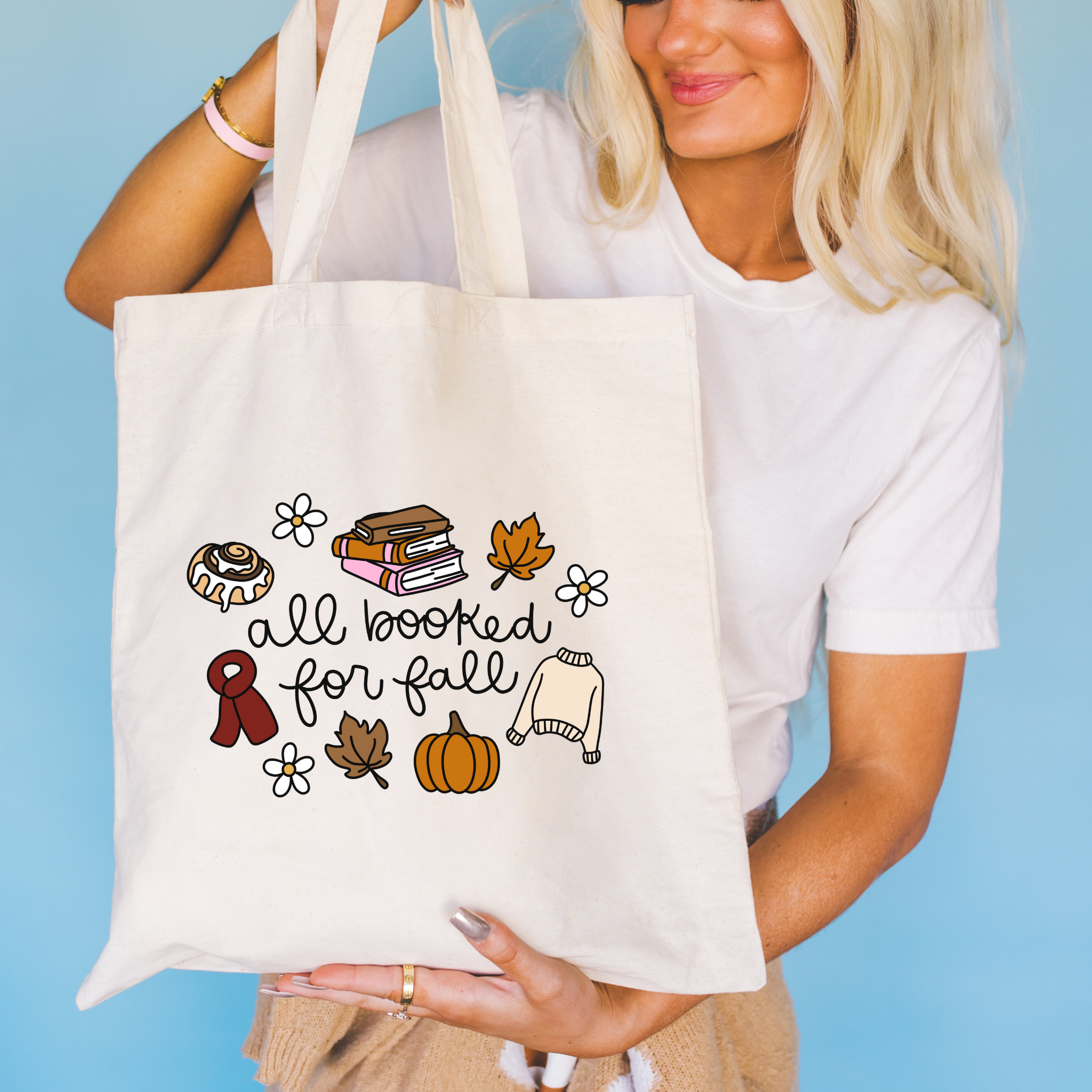 Person holding a tote bag with fall-themed illustrations and text against a blue background