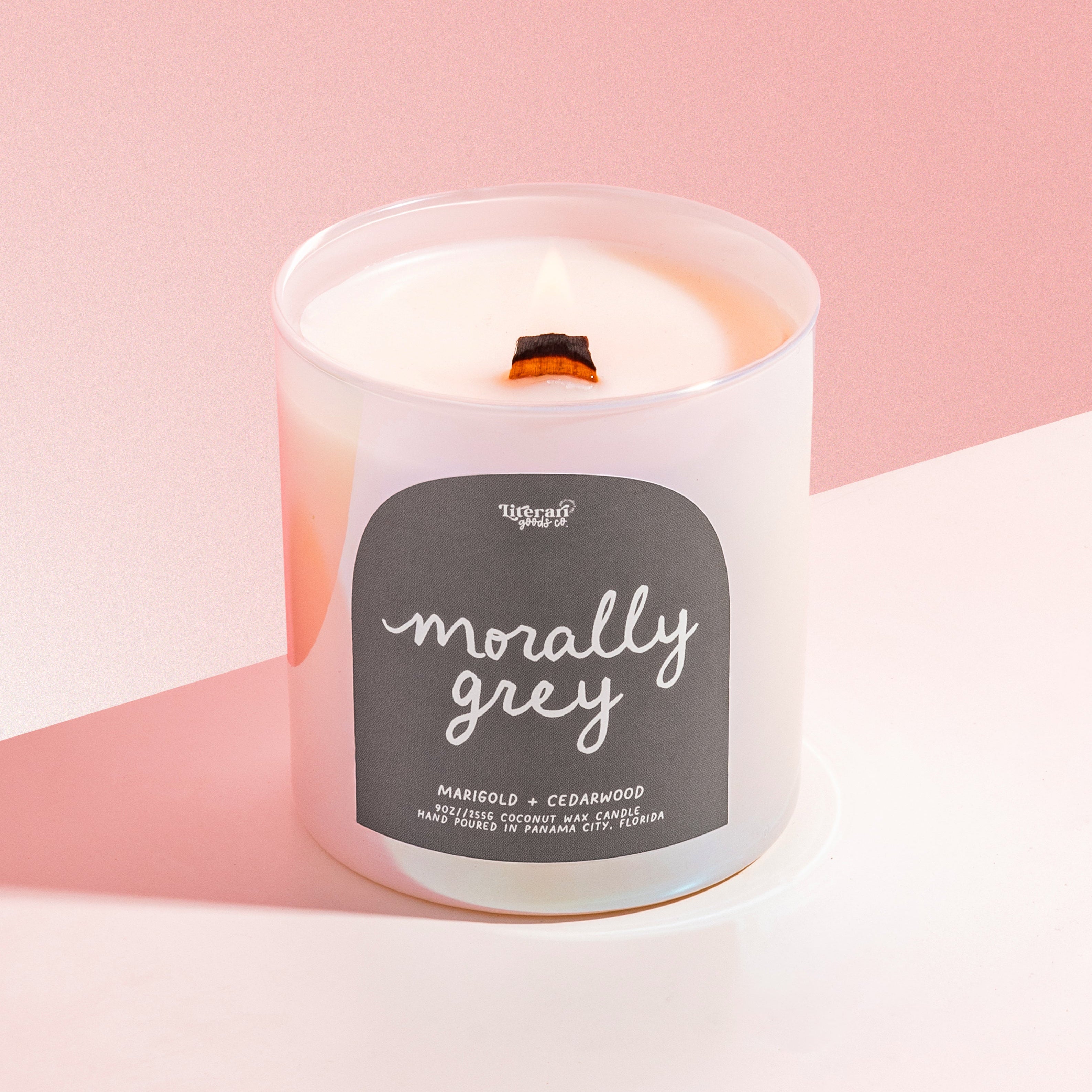 Book themed Candle with a label on a pink background, with label reading "morally grey"Bookish candle labeled “Morally Grey” with amber and sandalwood scent – Literari Goods