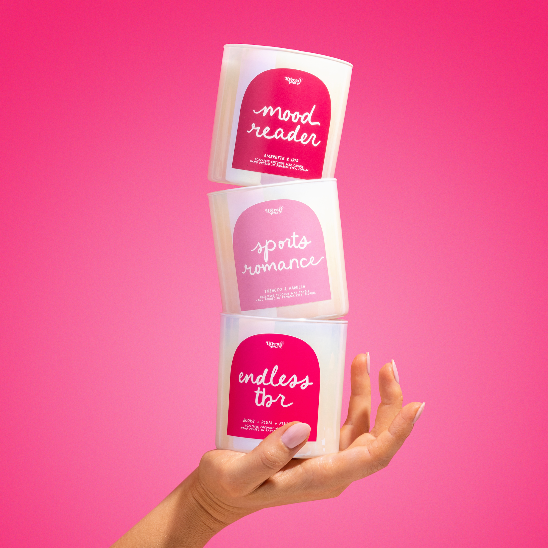 Three 'mood reader' bookish candles held by a hand against a pink background
