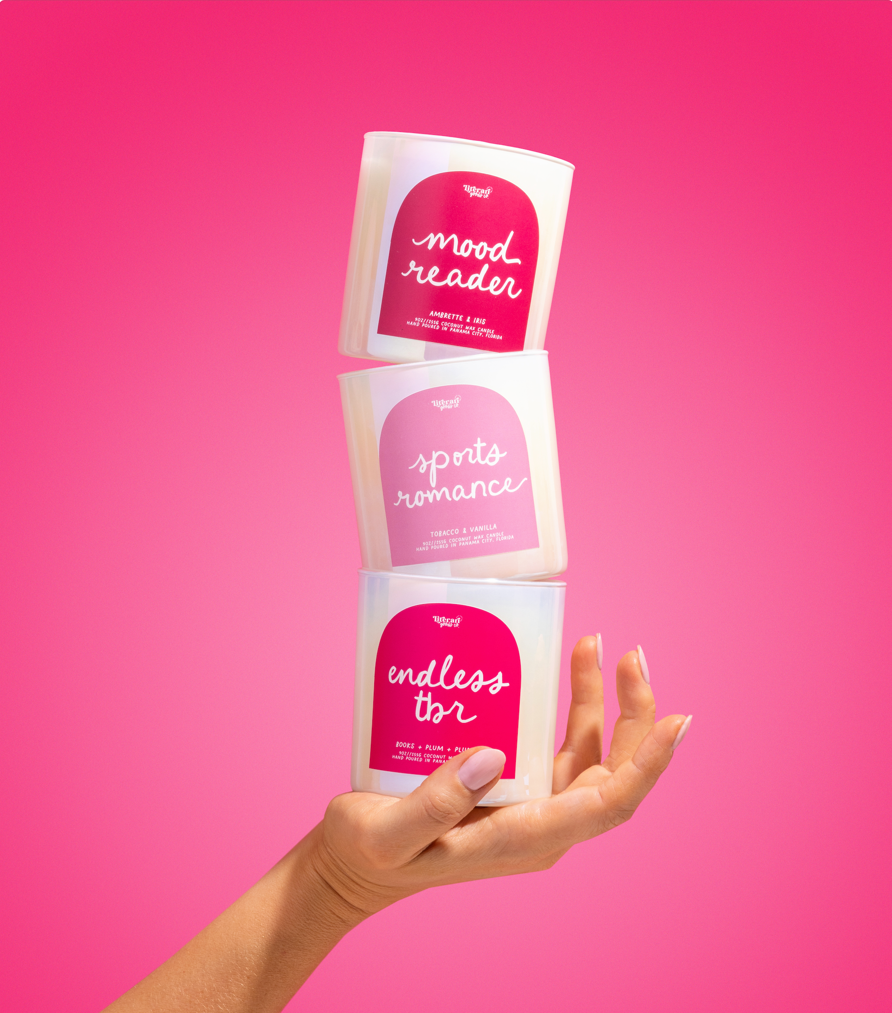 Three scented candles with labels 'mood reader', 'sparks of romance', and 'endless love' held against a pink background.